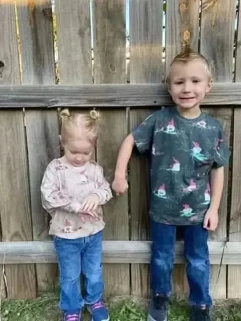 Two children wear shirts made from green and beige gnome toile fabric.