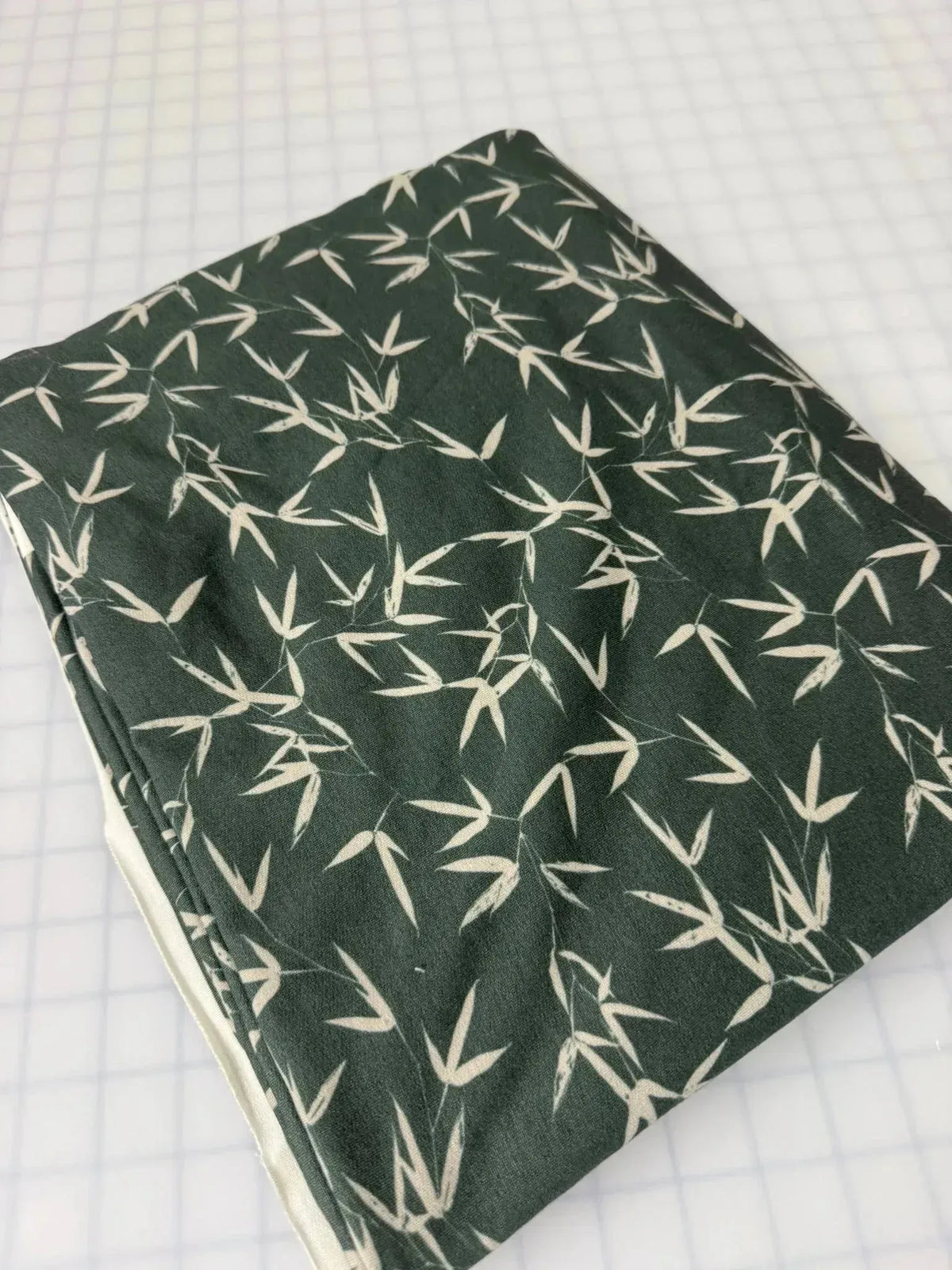 Green bamboo leaves print on fabric, folded on white background.