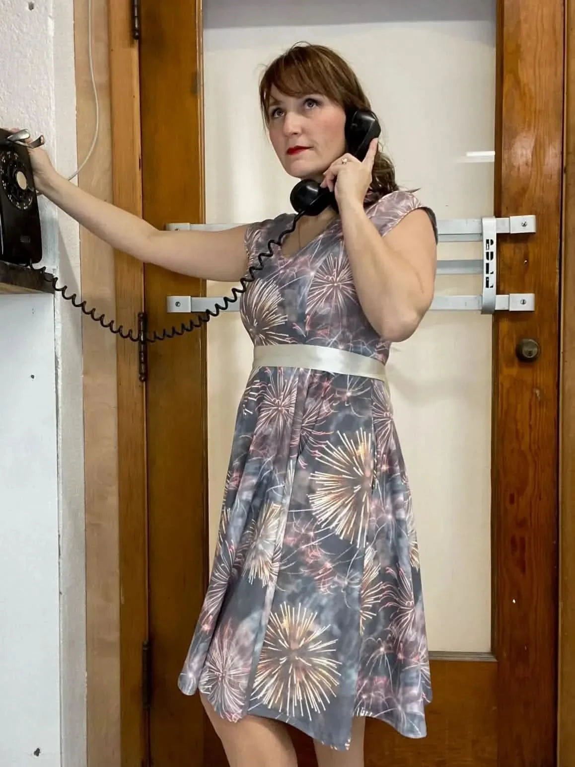 A woman in a Celebration print dress talks on a vintage black telephone.