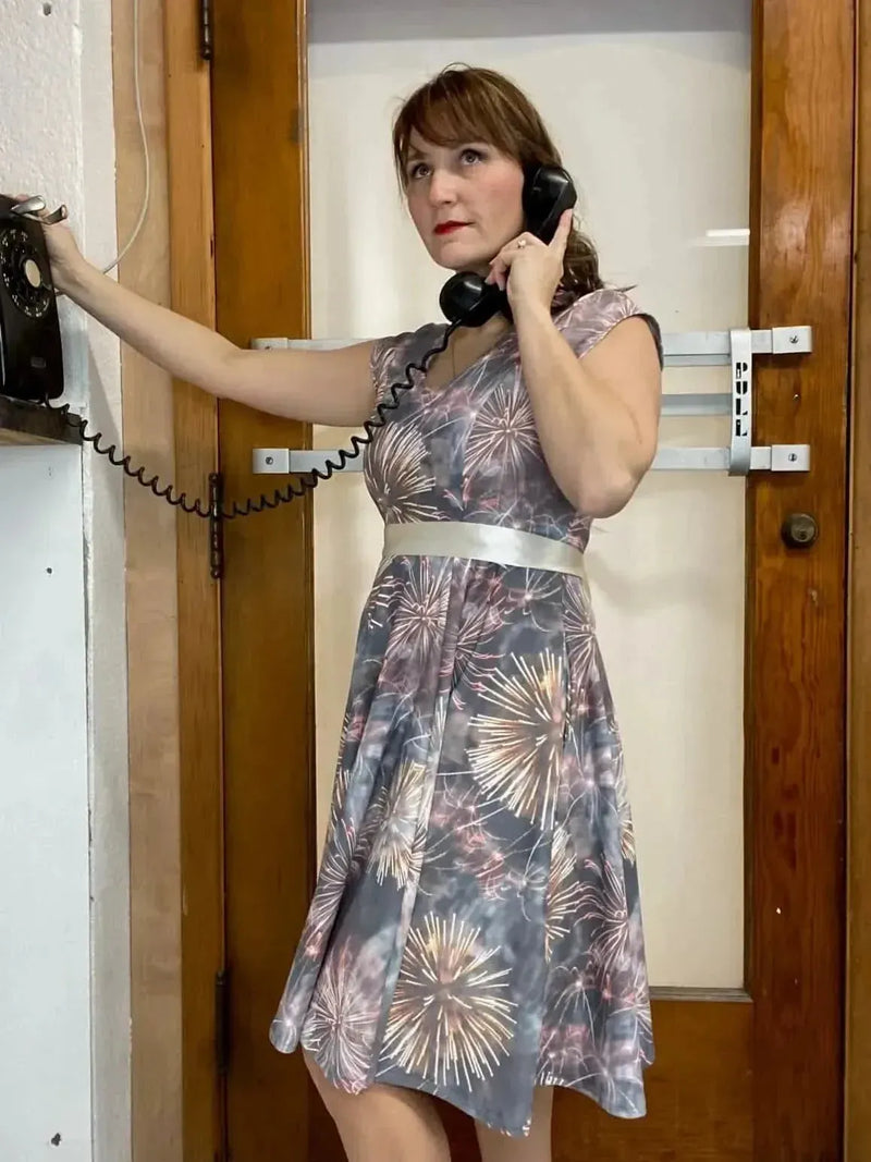 Woman modeling a gray sleeveless dress with colorful fireworks print, belted at waist.
