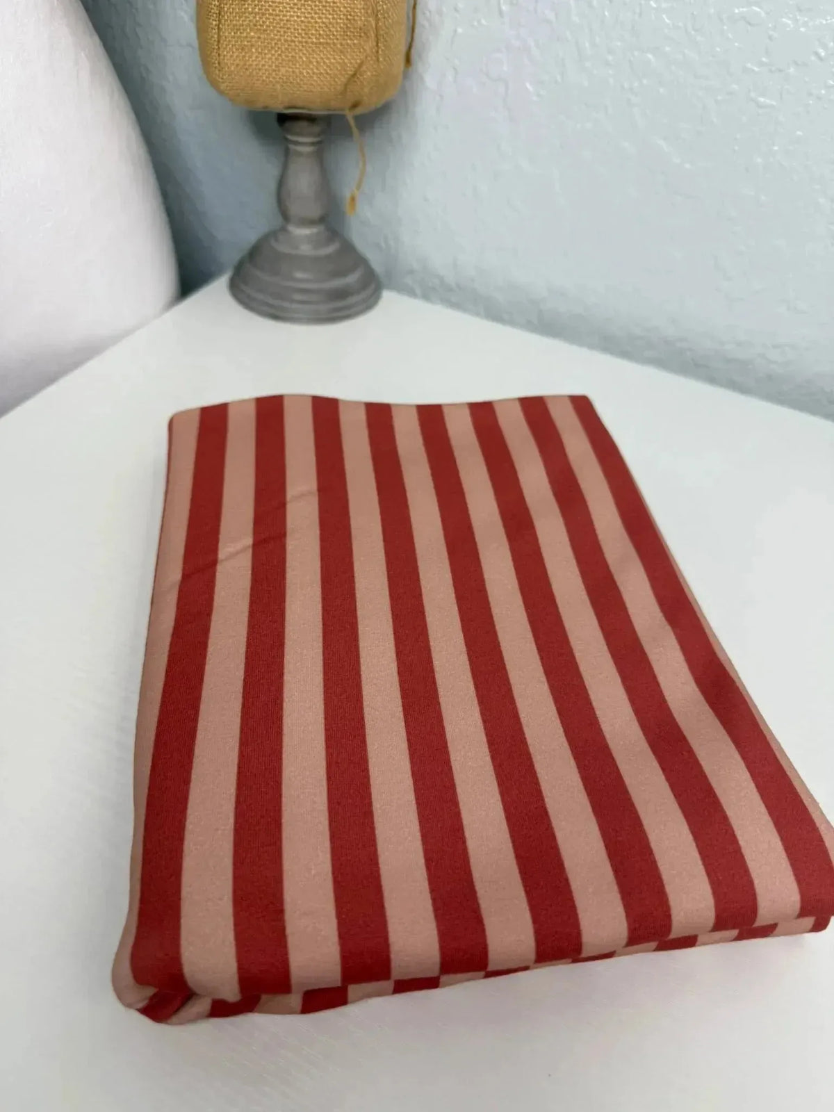 Folded neutral warm-toned striped fabric on a white surface with a lamp in the background.