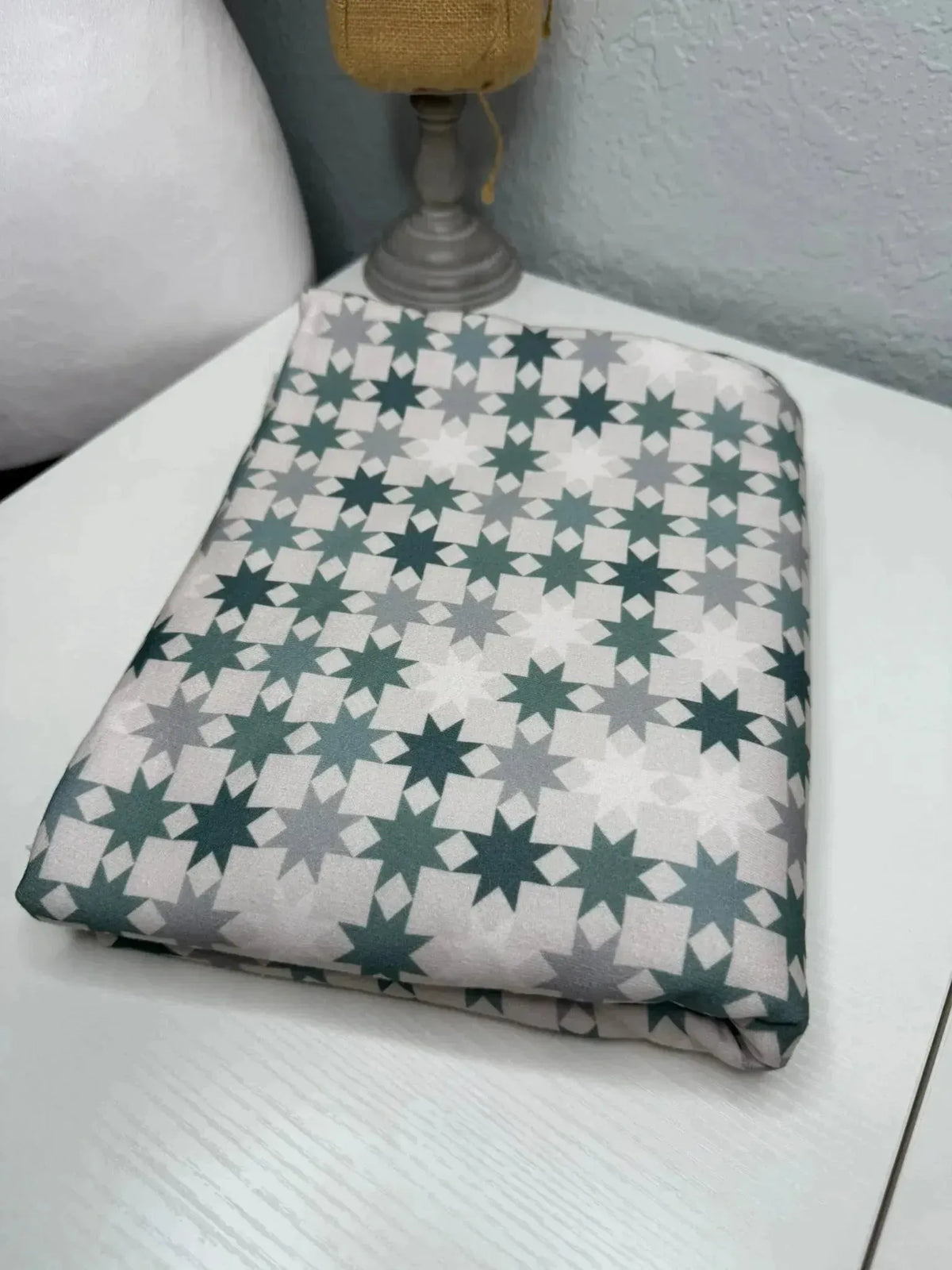 Green-grey geometric star print fabric folded on a white surface.