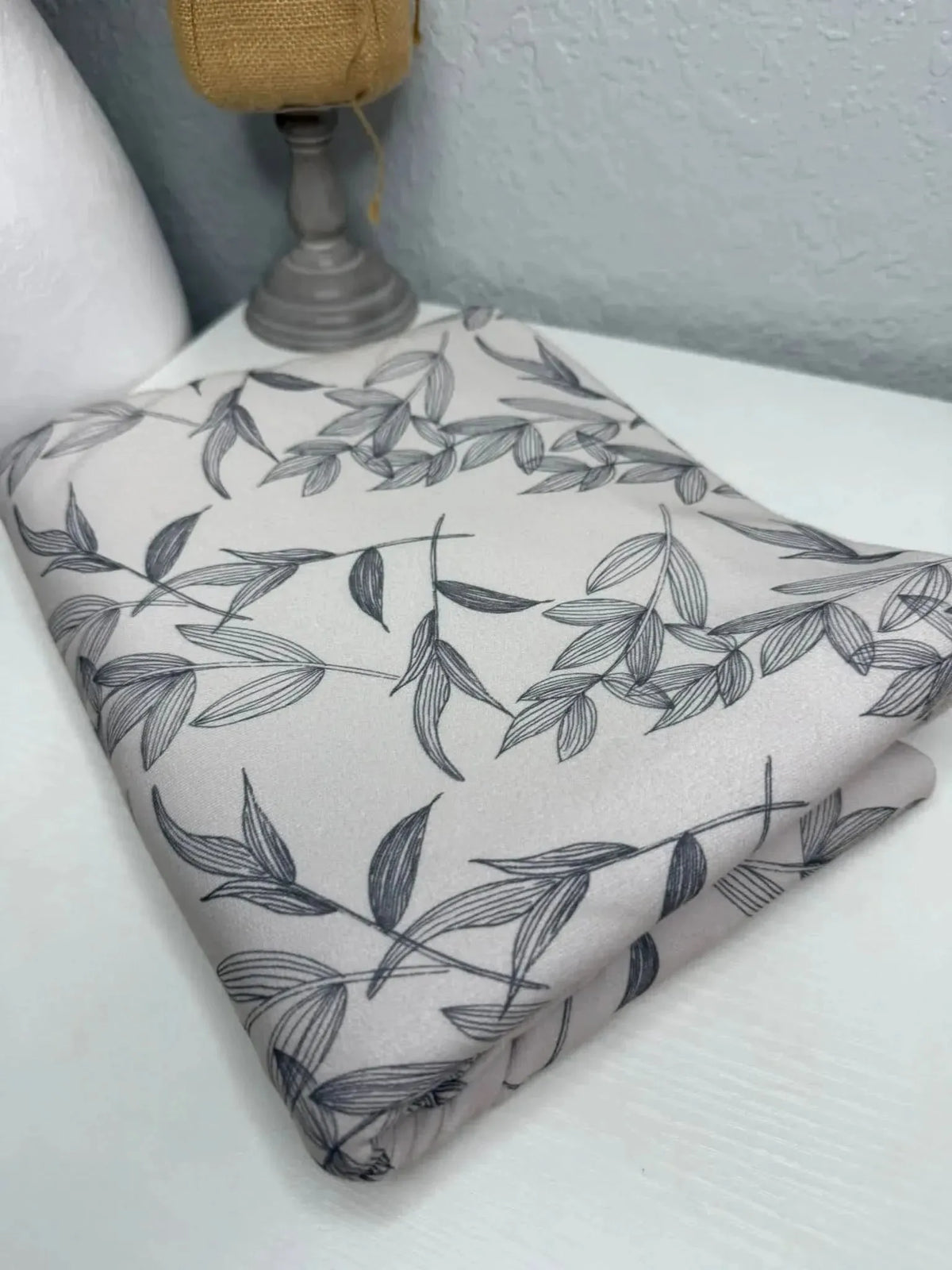 Grey botanical fabric with longing foliage print, folded on a white surface.