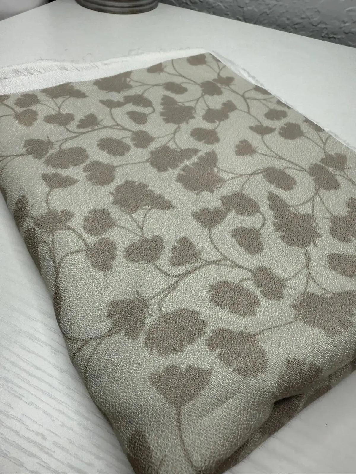 Beige fabric with subtle green leaf print pattern, folded on a white surface.