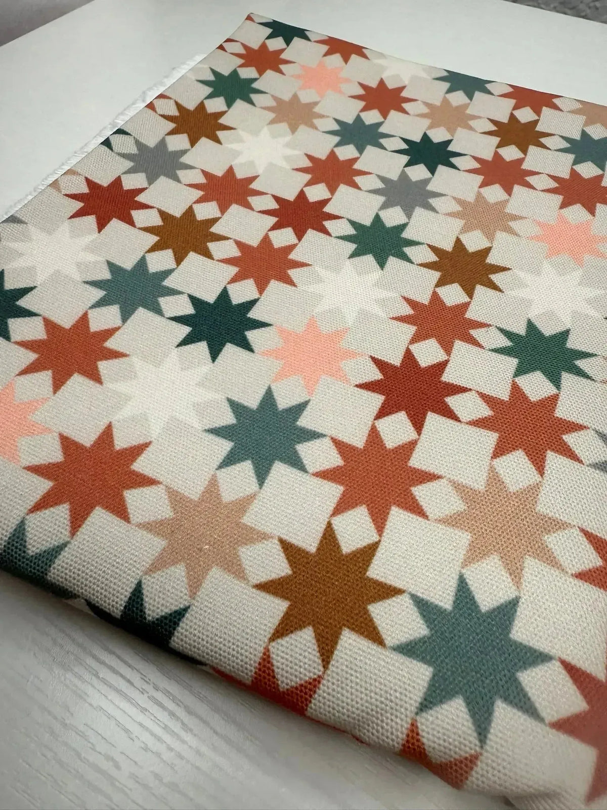 Fabric with geometric star pattern in earthy tones of green, pink, and brown.