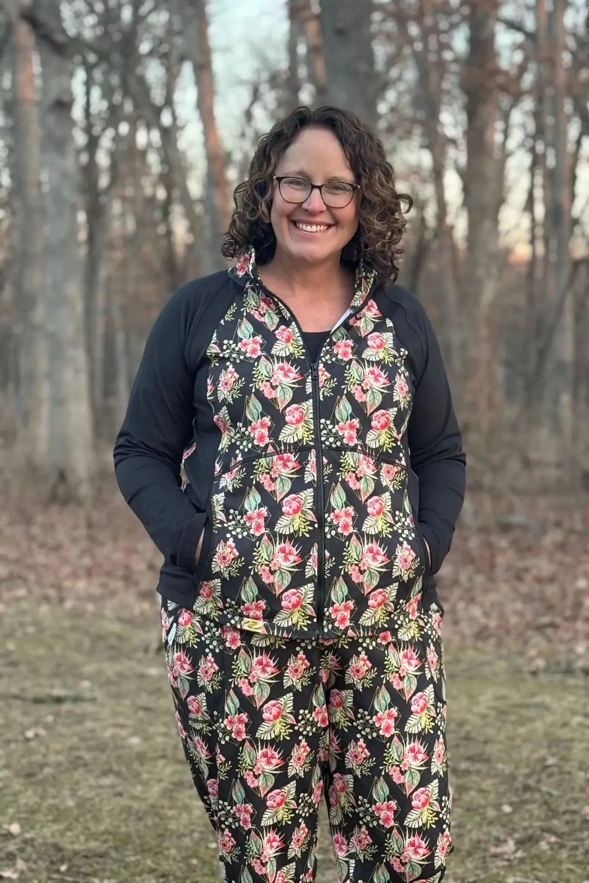 A woman smiles wearing a black floral print zip-up jacket and matching pants.