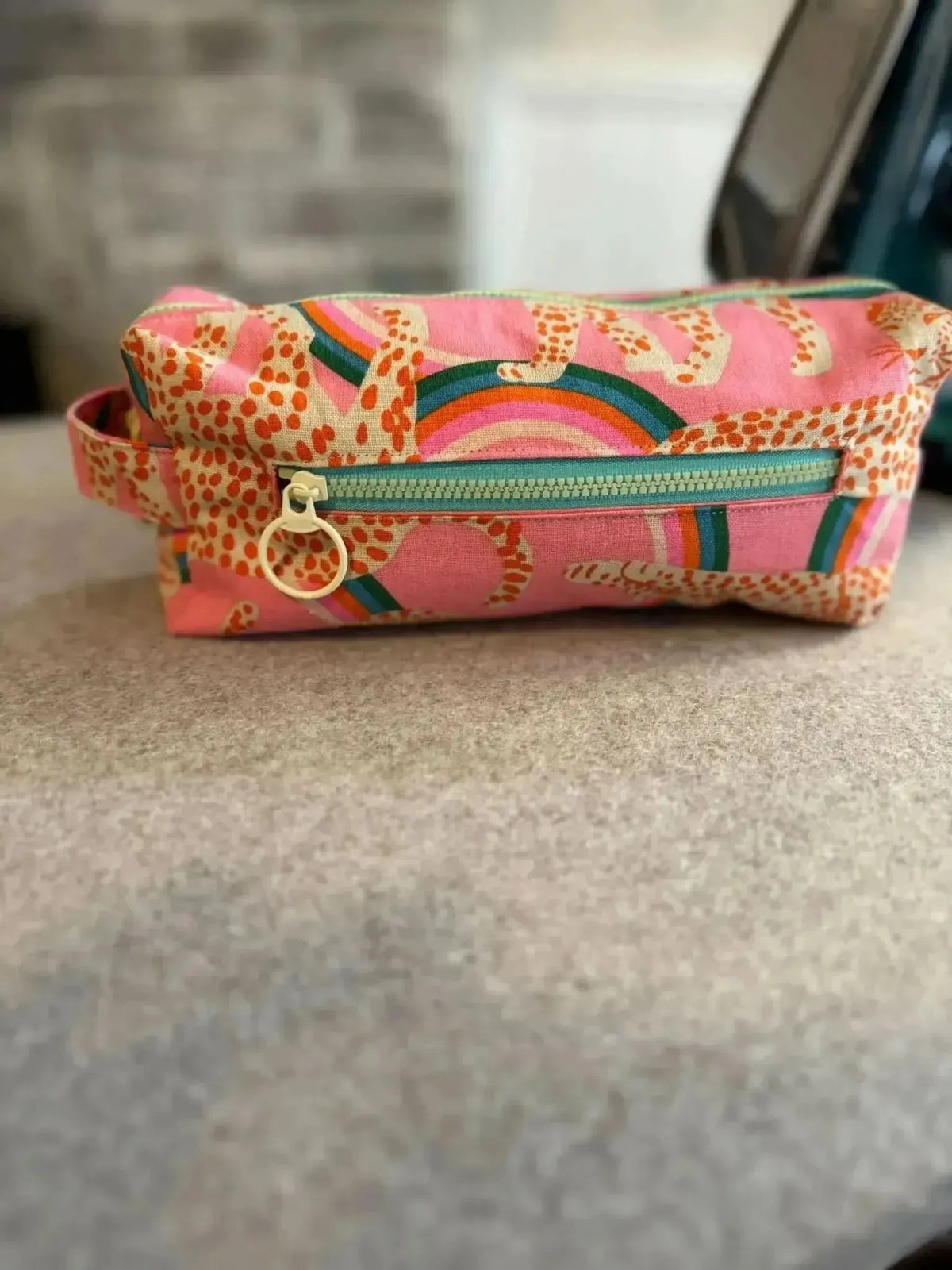 Pink zipper pouch with rainbow print, handle, and side pocket on gray surface.