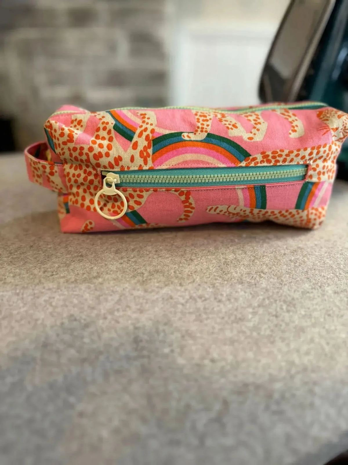 A pink and orange patterned zipper pouch with a light green zipper.