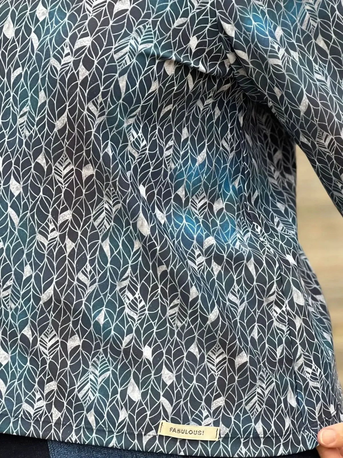 A person wearing a long-sleeved top with a silver leaf pattern on a dark background.