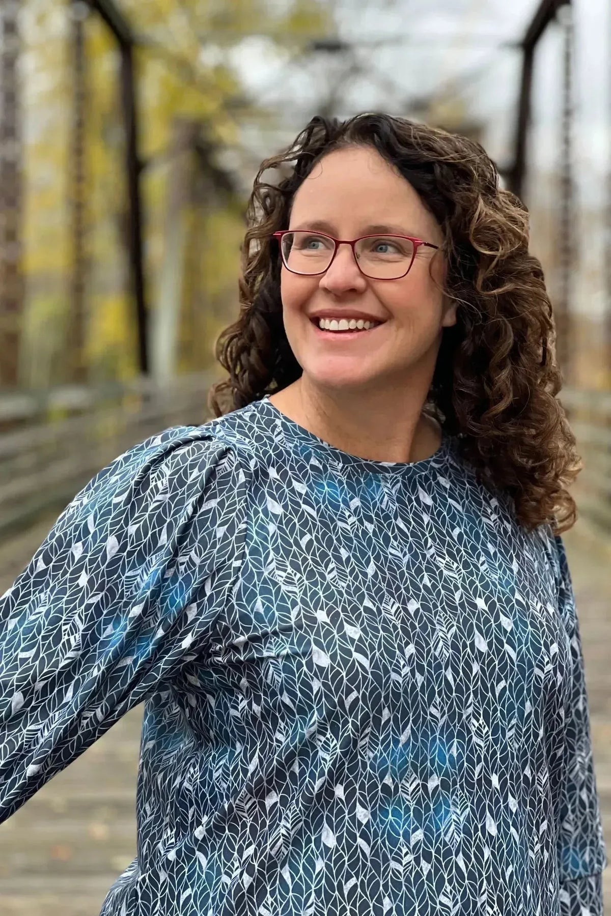 A woman wears a blue shirt with a white abstract leaf pattern.