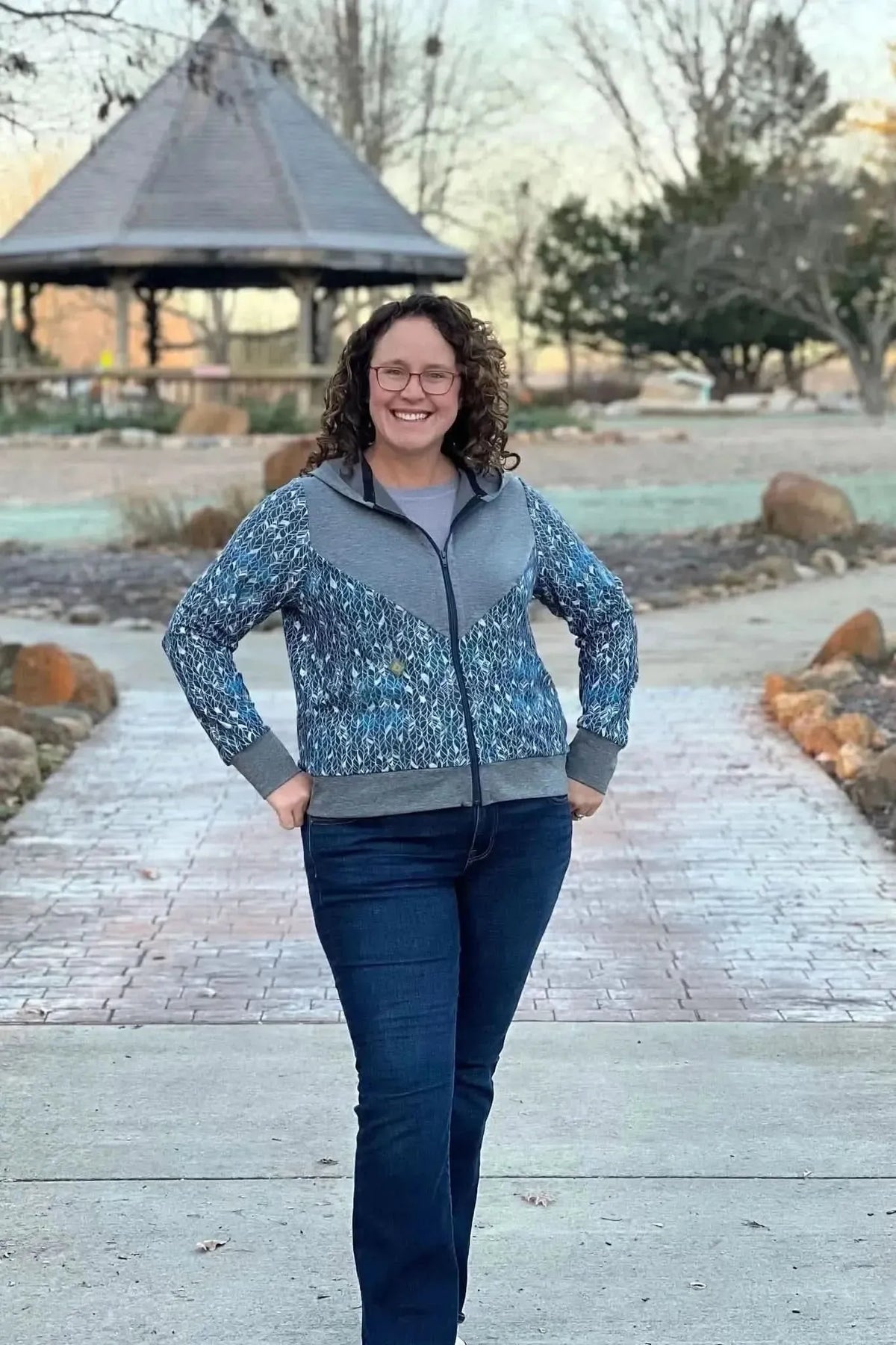 A woman wears a blue and gray jacket with an abstract leaf pattern.