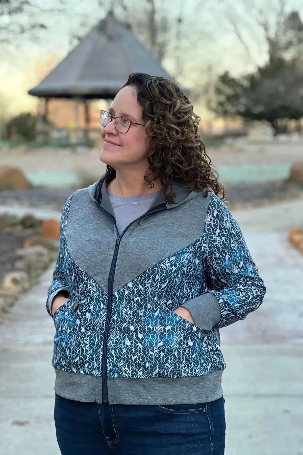 Woman wearing a blue and gray zip-up jacket with a silver leaf pattern.
