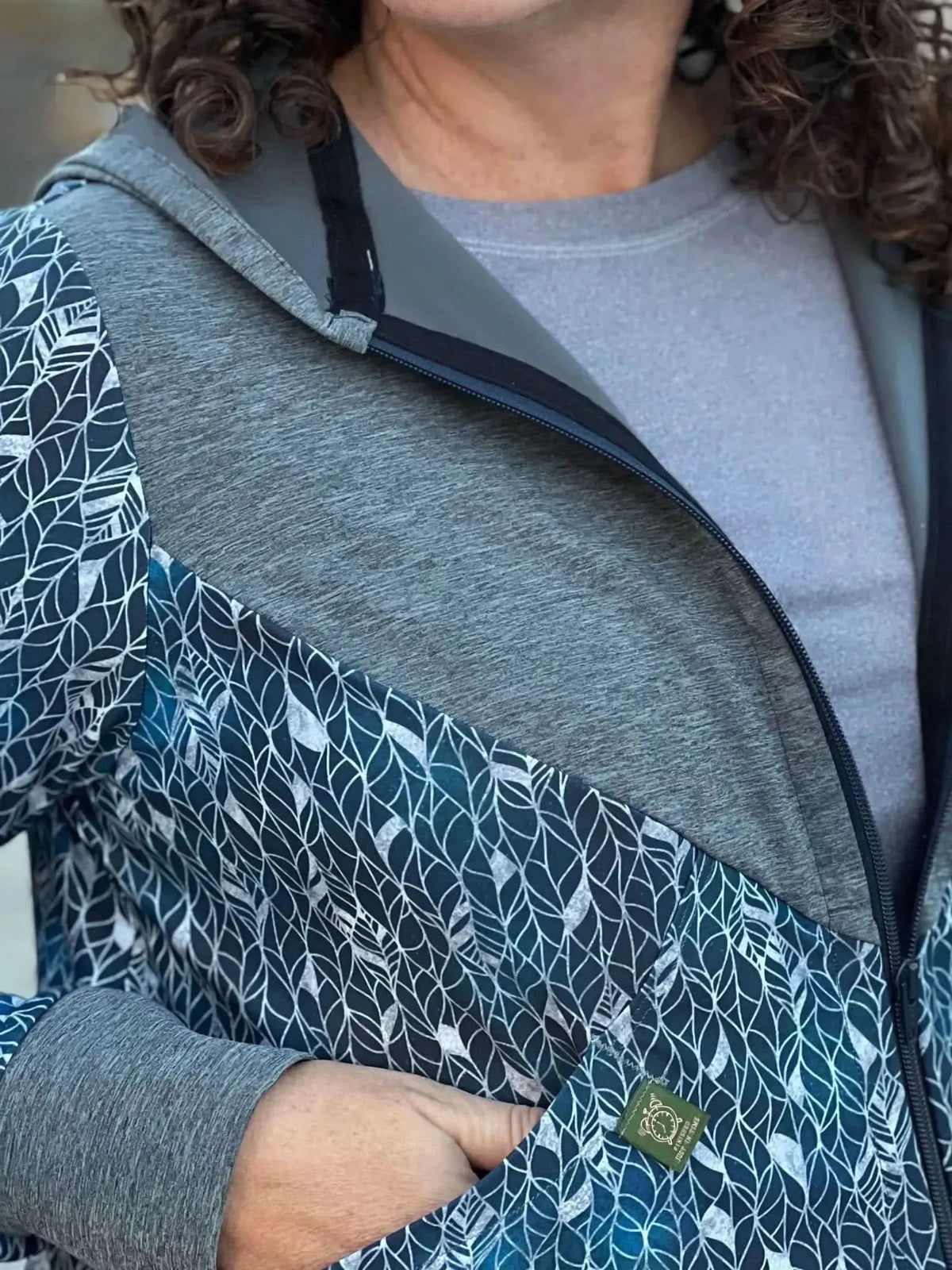 A person wearing a blue and gray hoodie with a silver leaf pattern.
