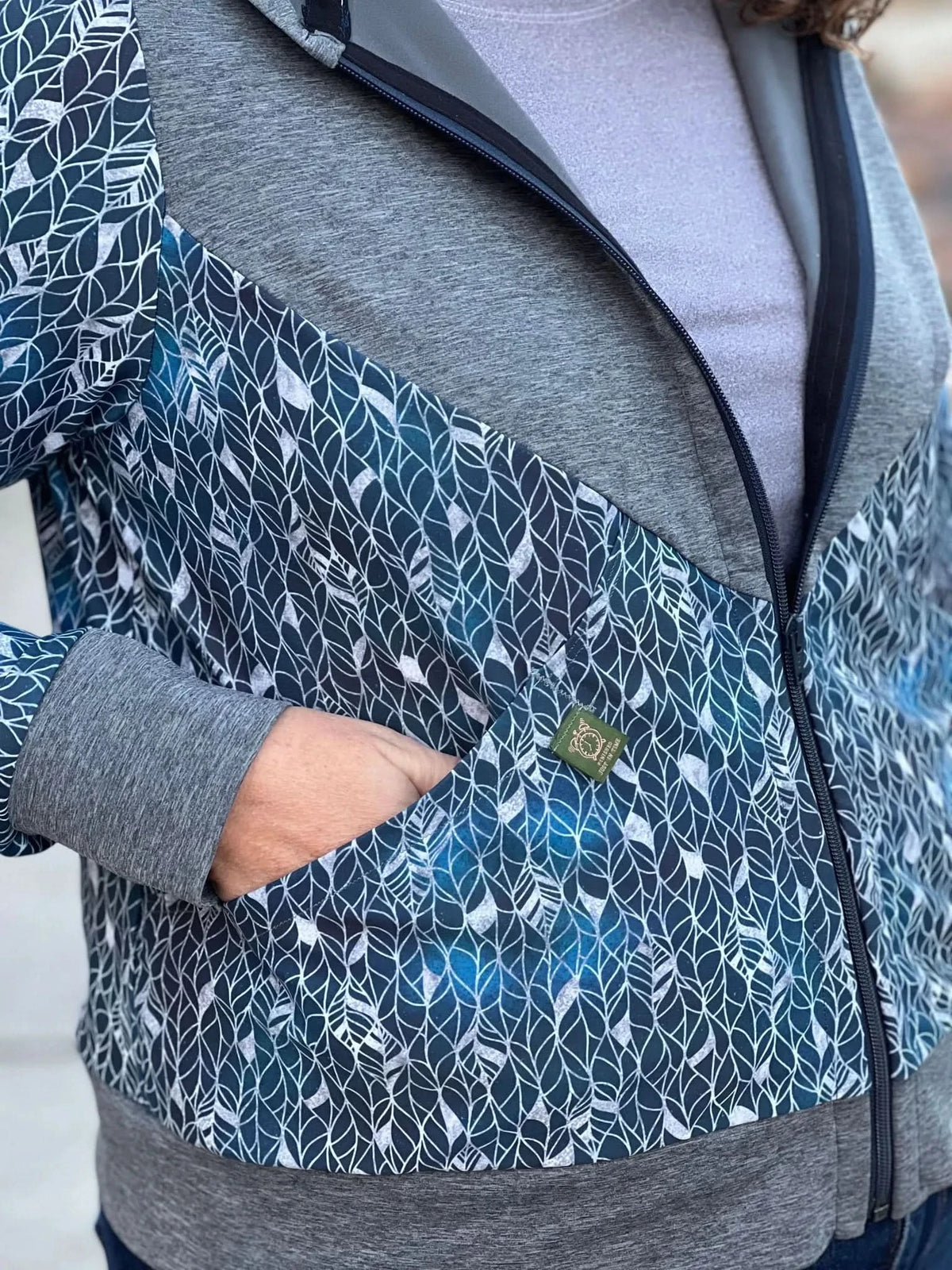 A person wearing a blue and gray zip-up jacket with a leaf pattern.