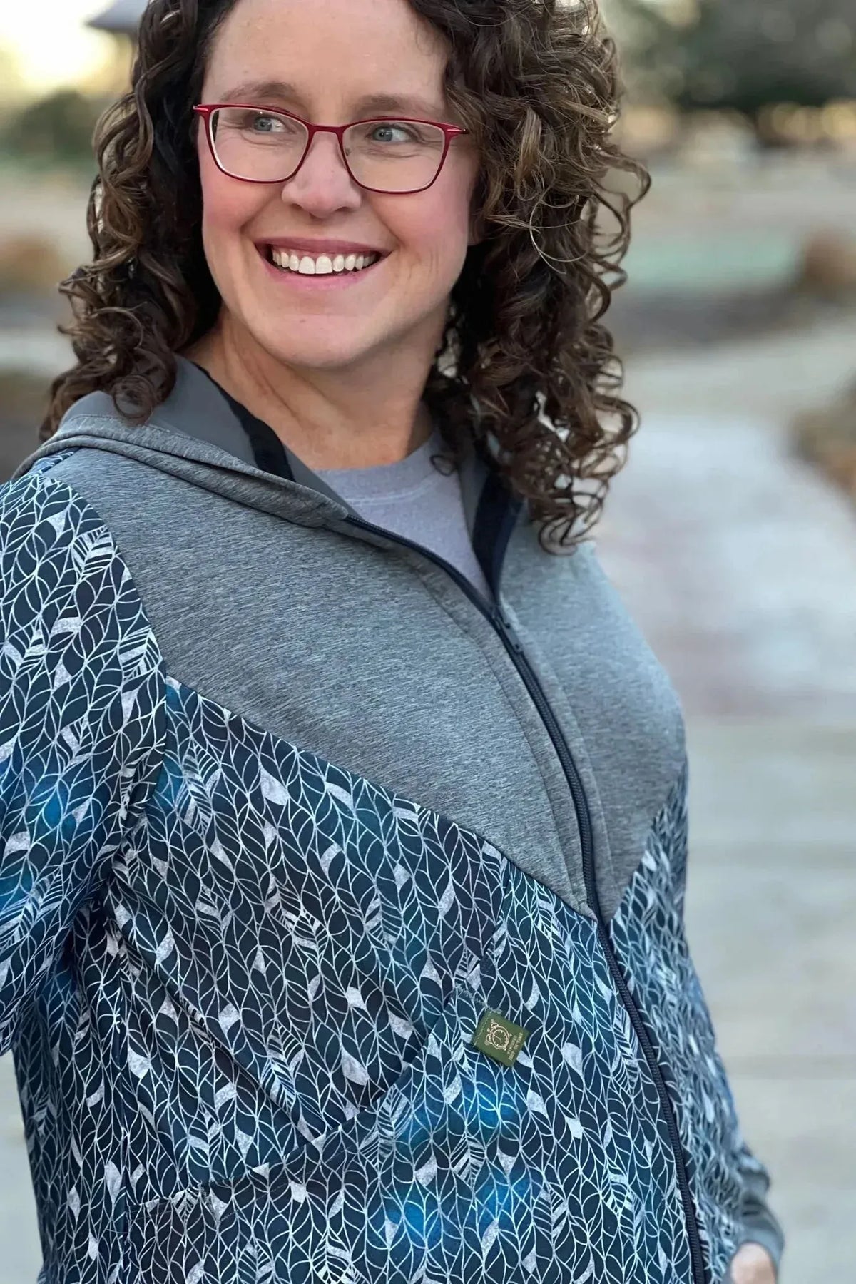 Woman wearing a gray hoodie with silver abstract leaf pattern print.