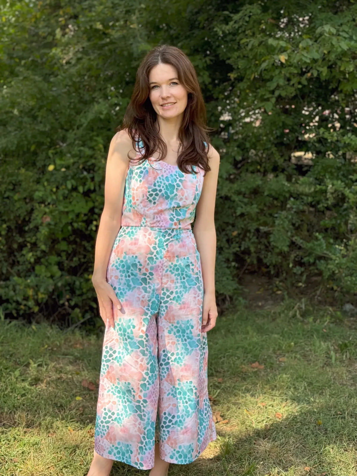 Woman in a colorful, patterned jumpsuit stands outdoors.