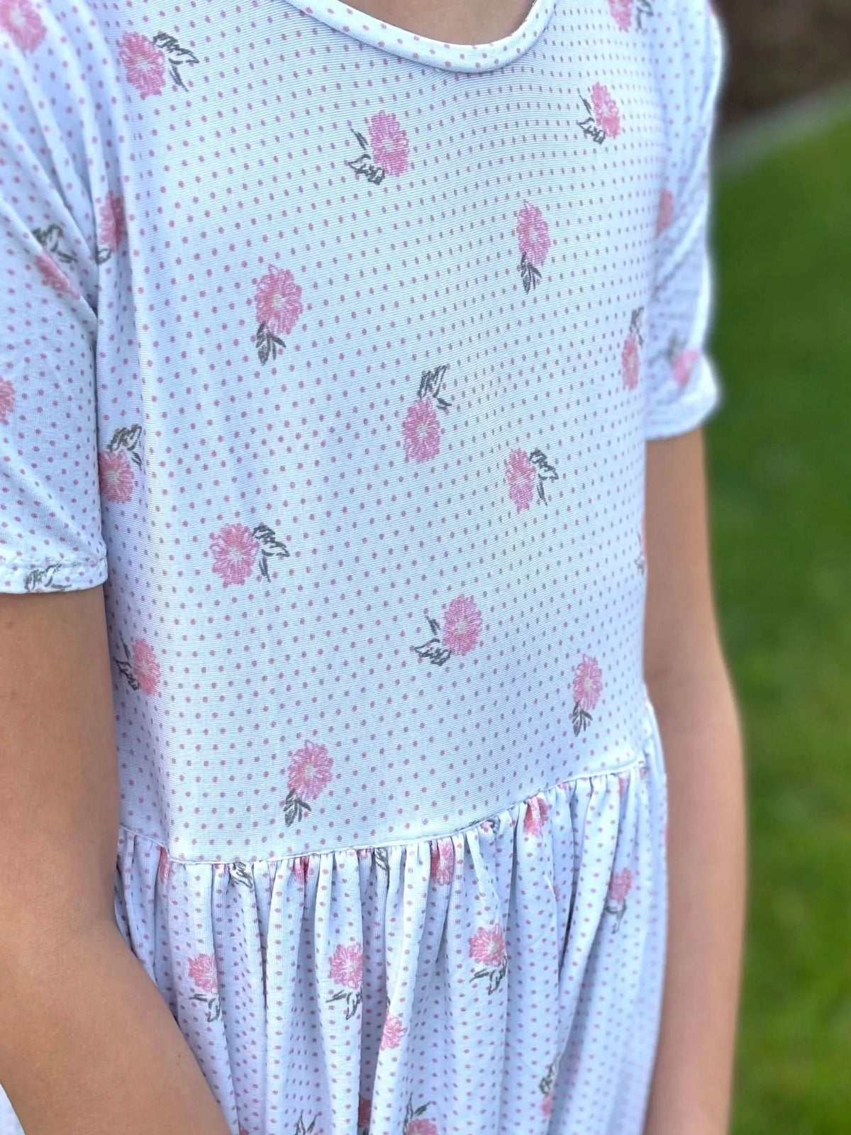 A child wears a white dress with pink polka dots and floral patterns.