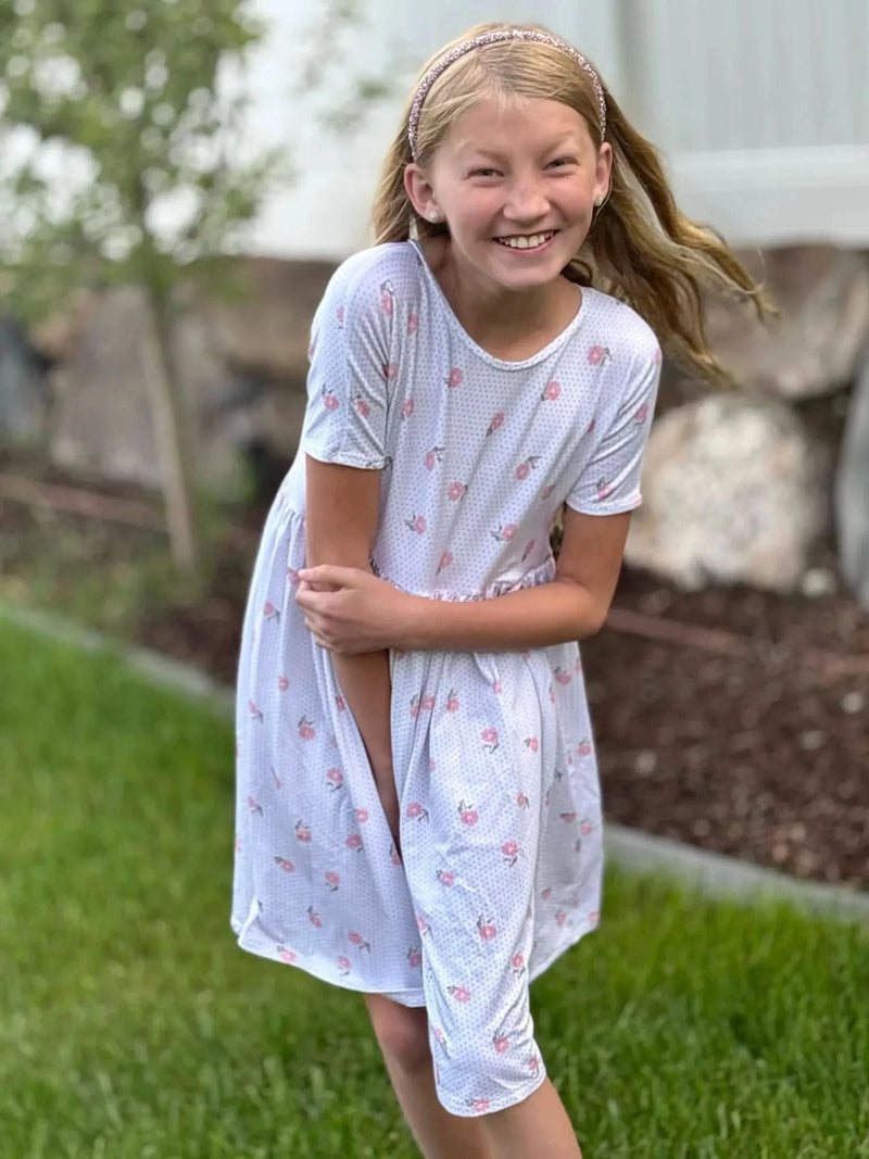 A girl in a white dress with pink floral and polka dot print.