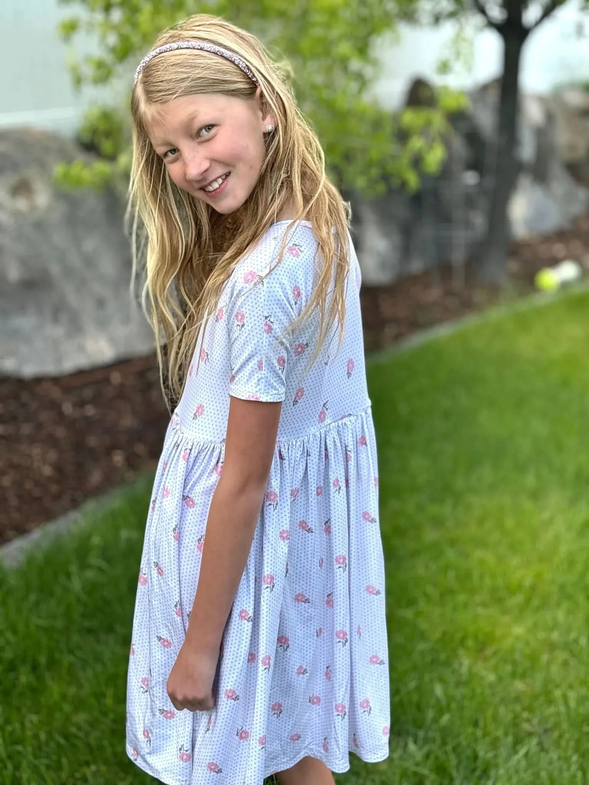 A young girl in a white dress with pink floral and blue polka dot print.