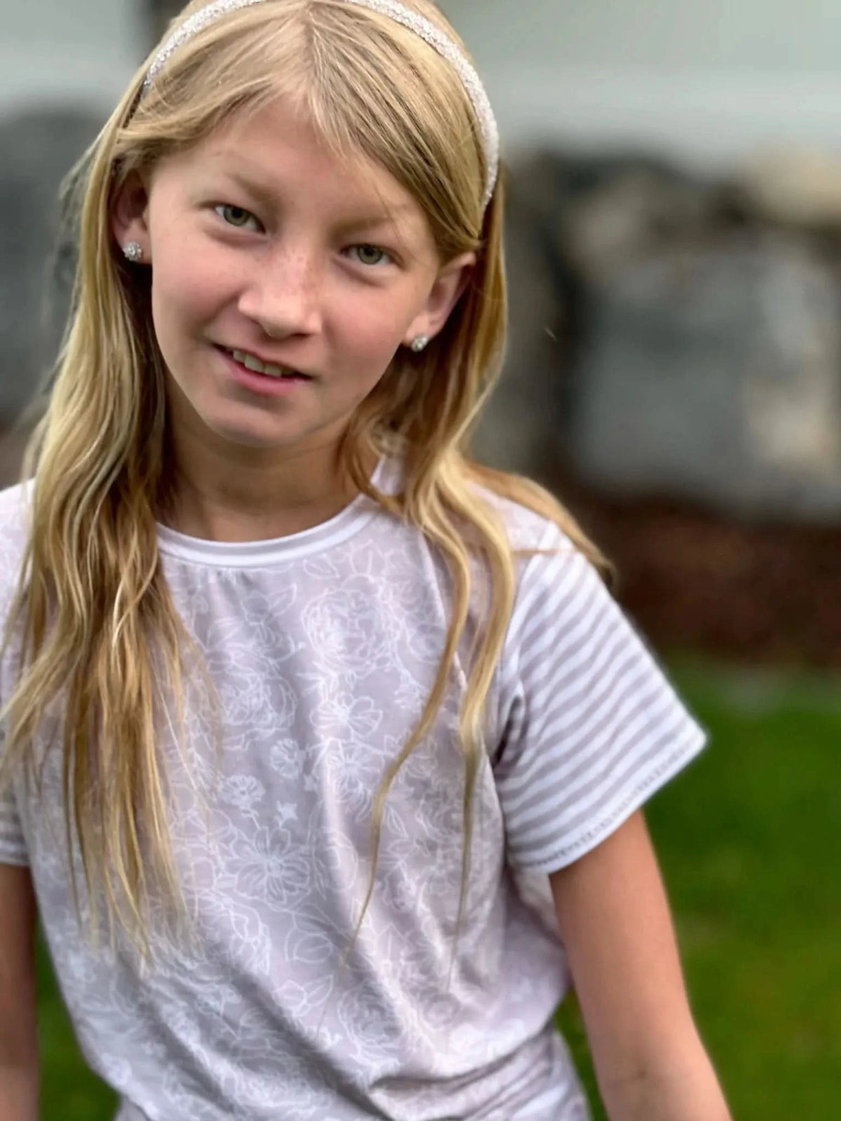 A young girl wears a tan stenciled floral shirt with striped sleeves.