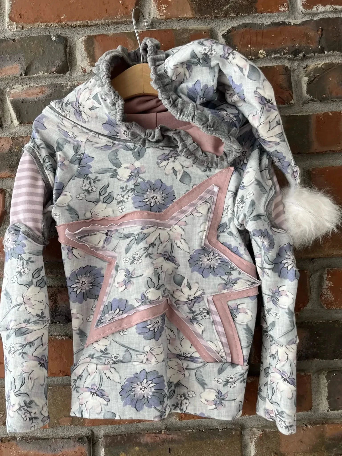 A floral hoodie with a star design and a hood with a white pom-pom.