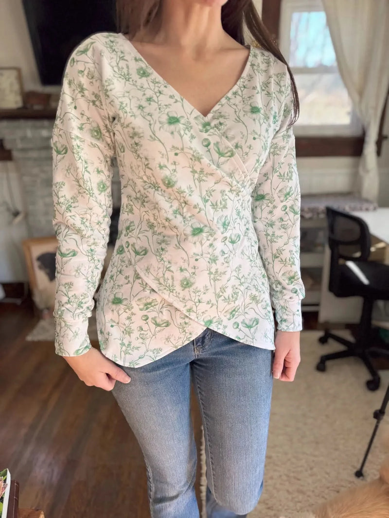 A woman wears a white wrap top with a green floral pattern and blue jeans.