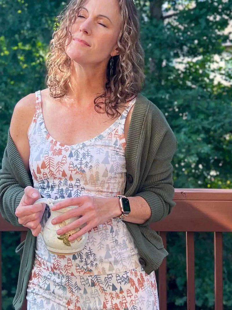 A woman wears a tank top with a light fall tree pattern and a green cardigan.