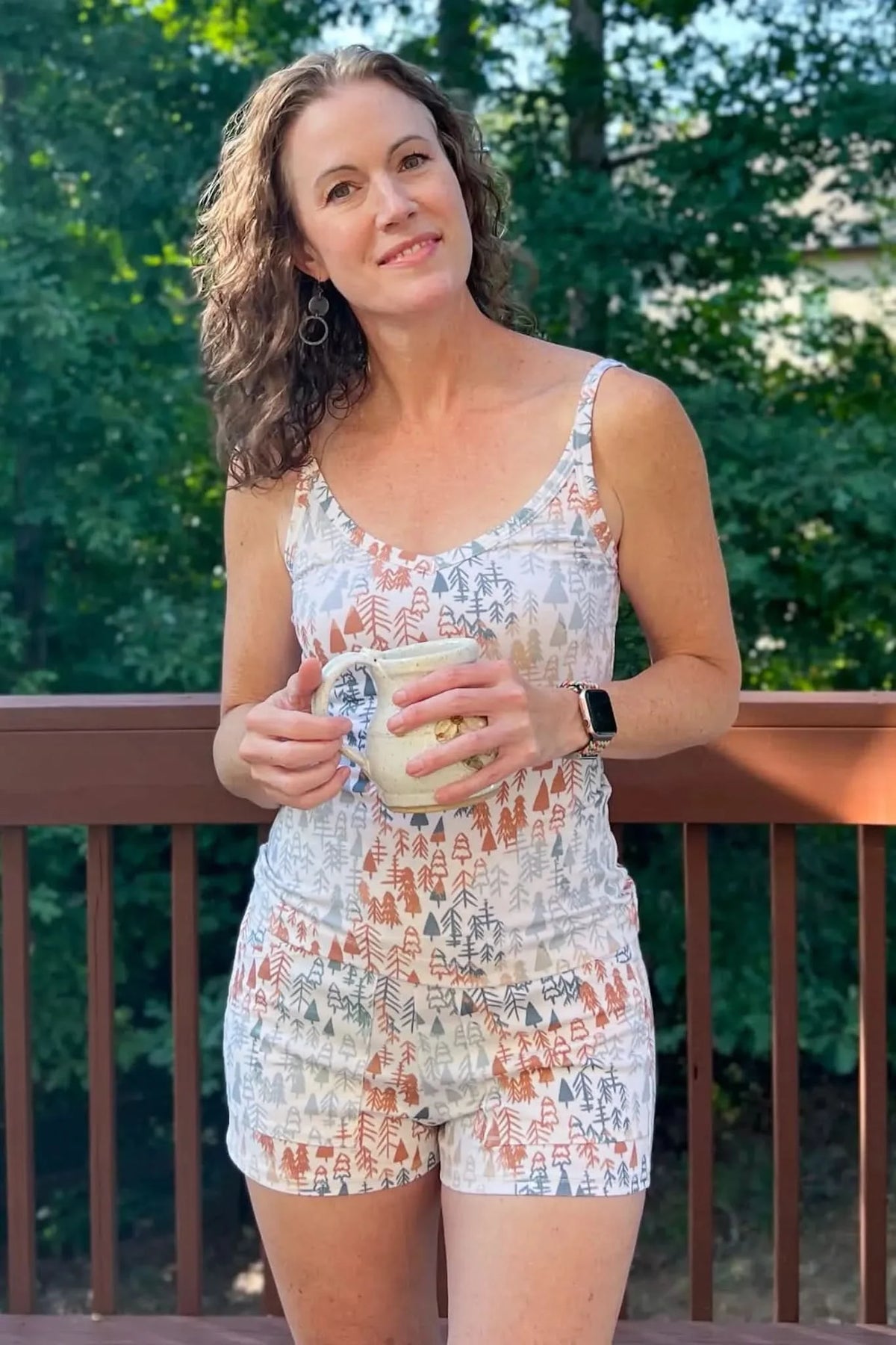 A woman wears a tank top and shorts with a light fall trees pattern.