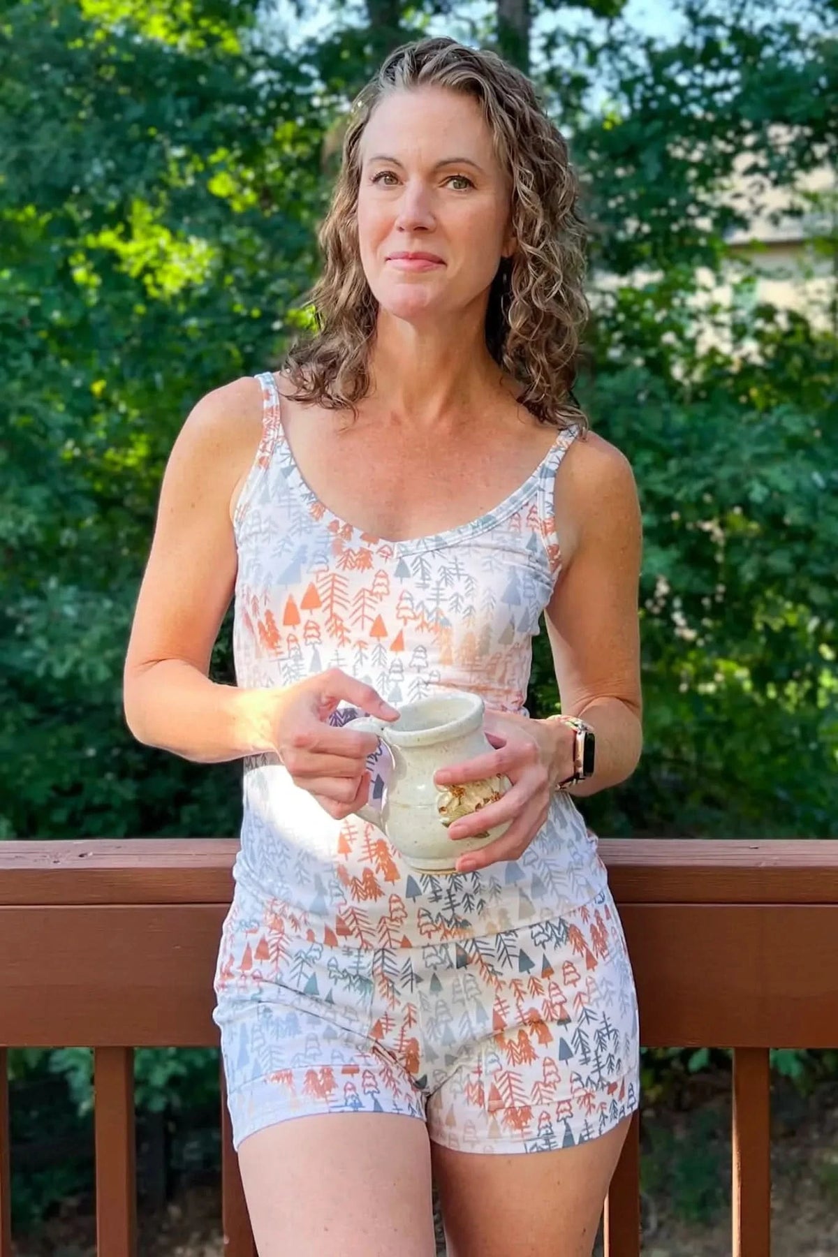 A woman wears a tank top and shorts with a light fall trees pattern.