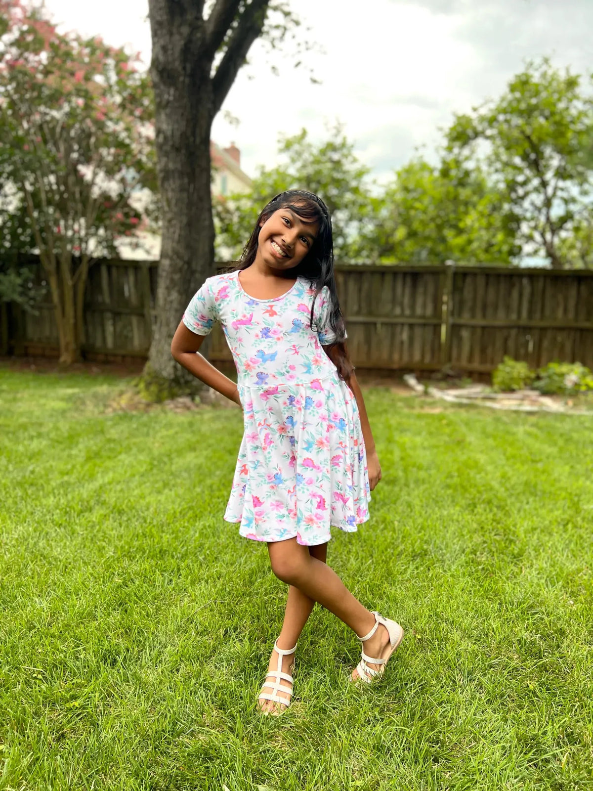 A girl in a white dress with colorful dinosaur and floral patterns.