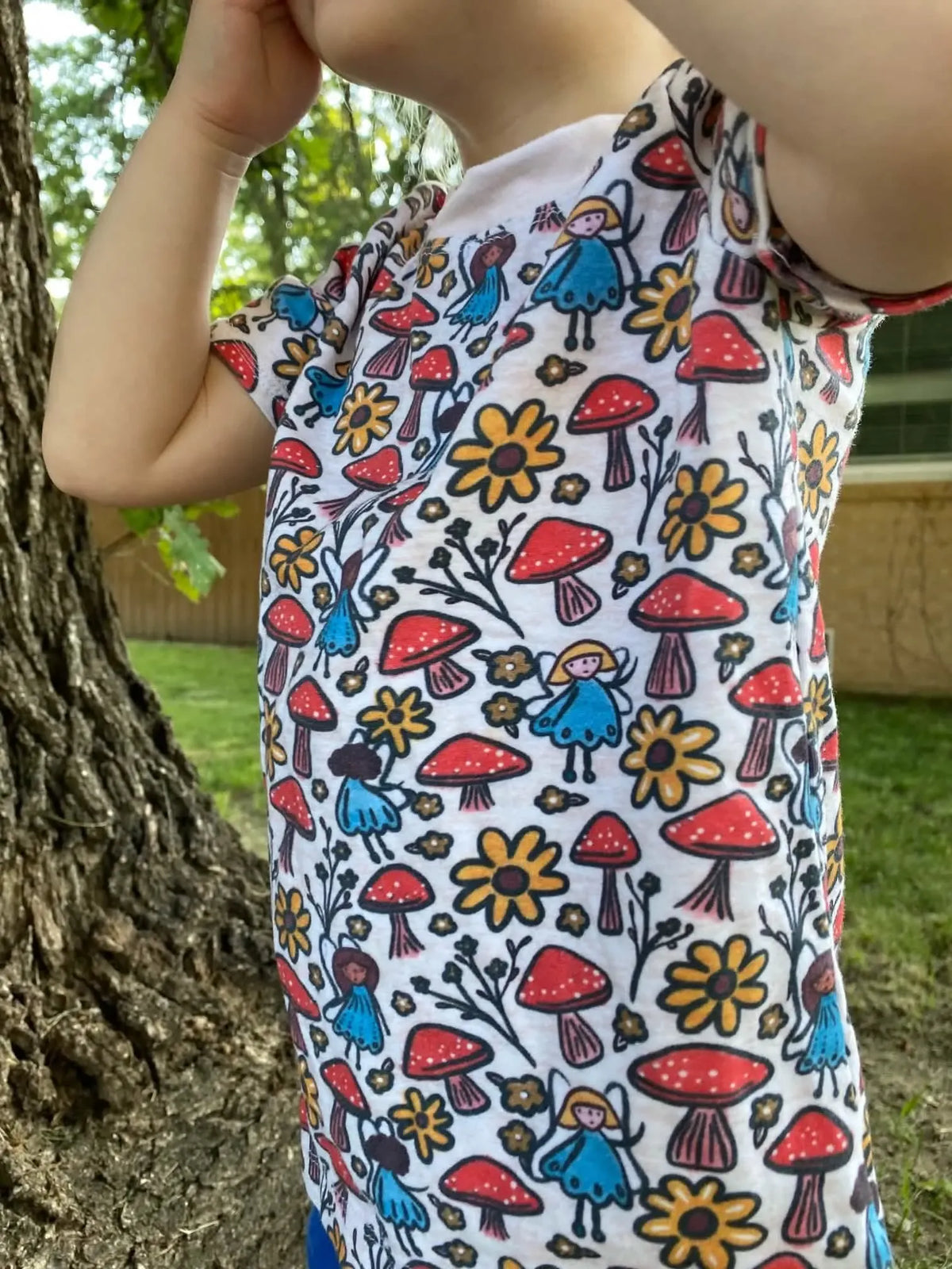 Child in a white shirt with a colorful mushroom and fairy print.