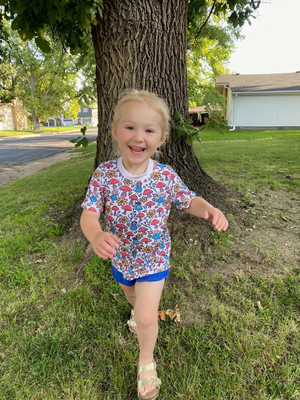 A young child wears a white shirt with a colorful mushroom and flower pattern.