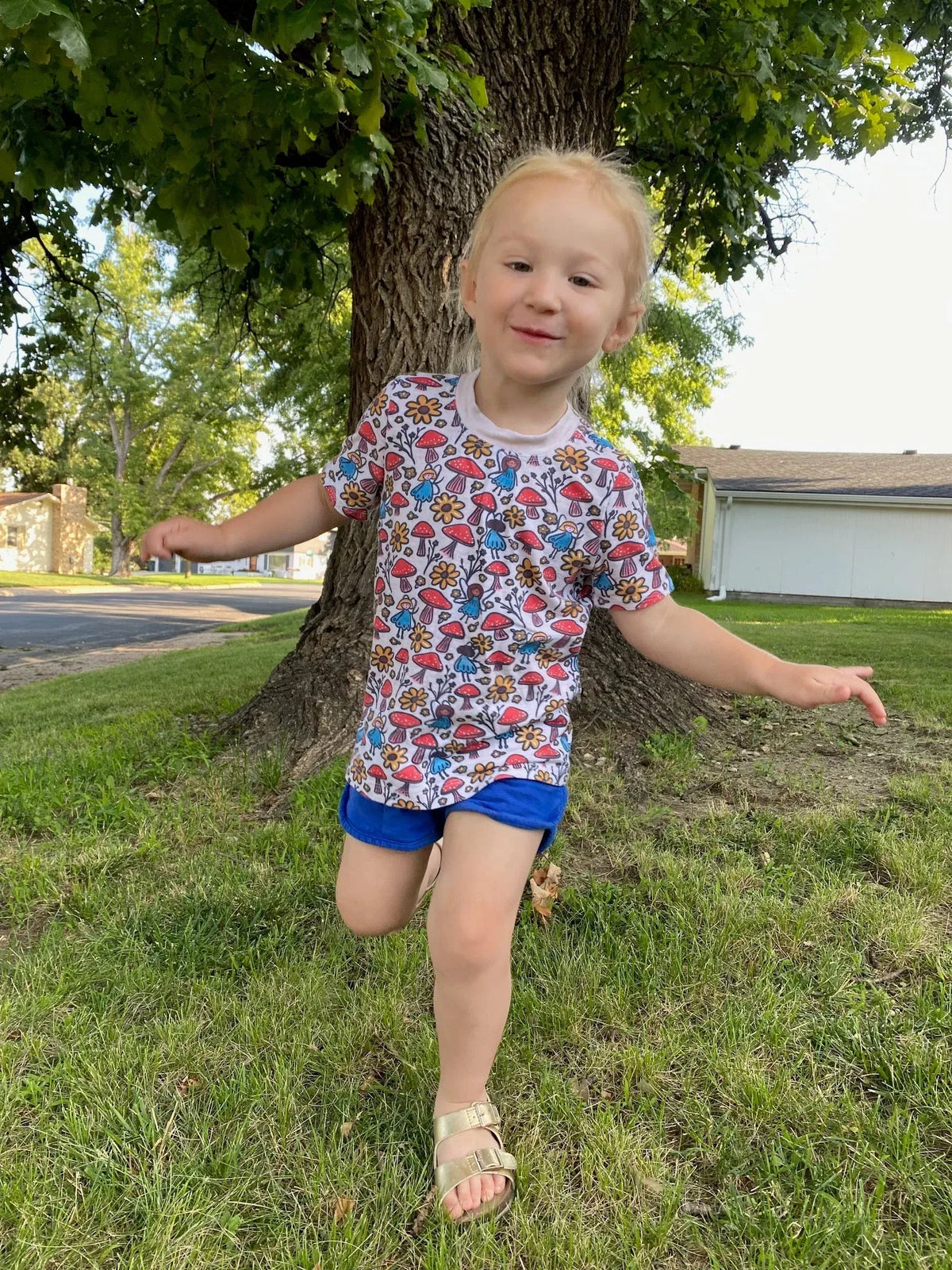 A young girl in a white shirt with a colorful mushroom and flower pattern.