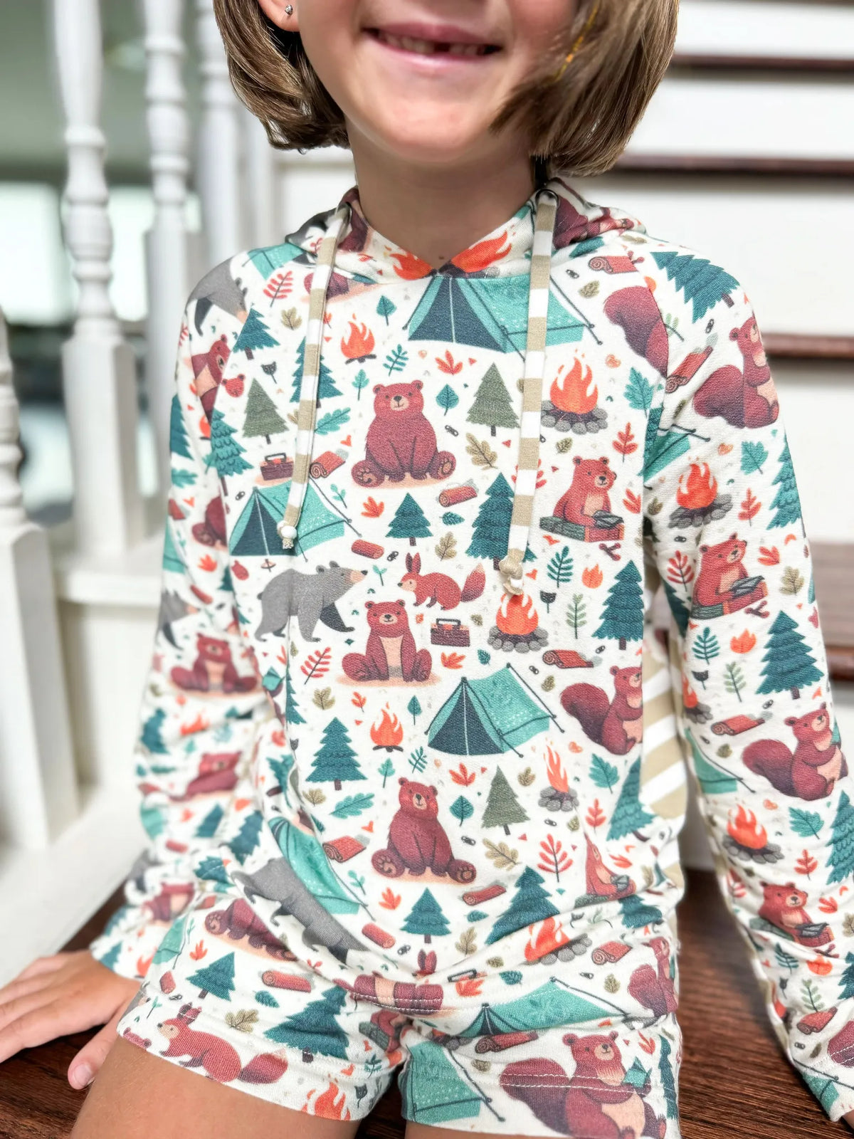 Child wearing a long-sleeved hoodie and shorts with a camping bears print.