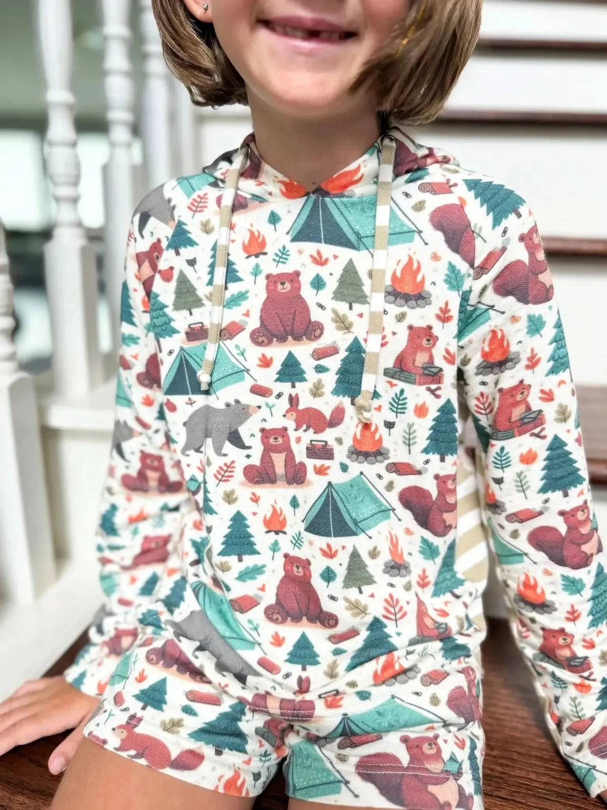Child wearing a long-sleeved hoodie and shorts with a camping bears print.