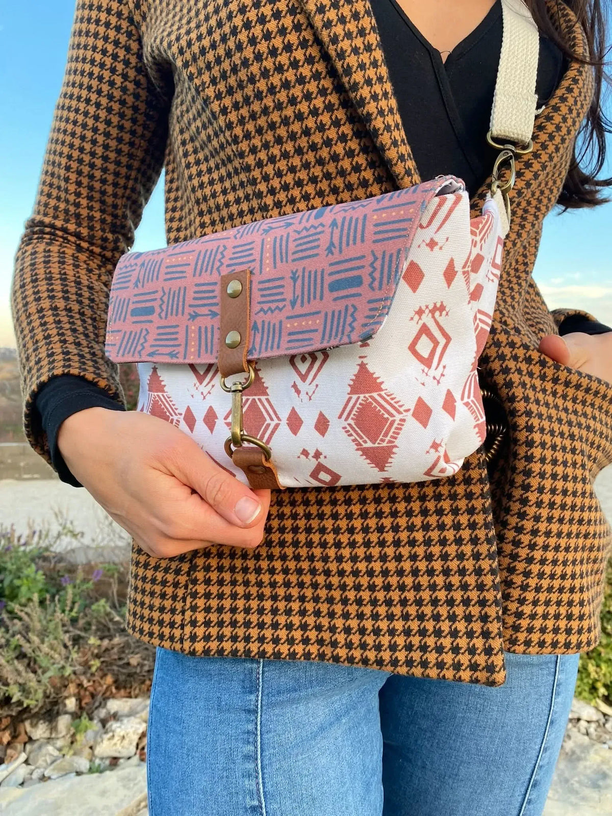A person in a houndstooth jacket and jeans holds a patterned fabric bag.