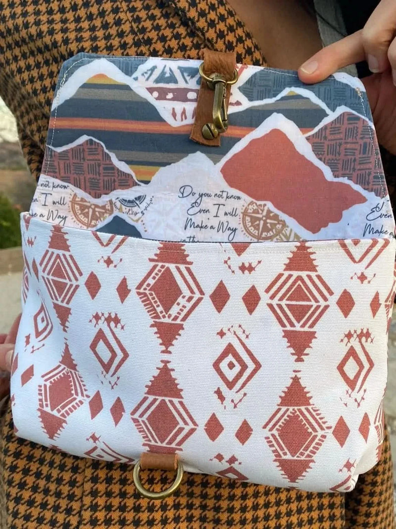 A person holds open a bag with a desert-themed flap and geometric pattern.