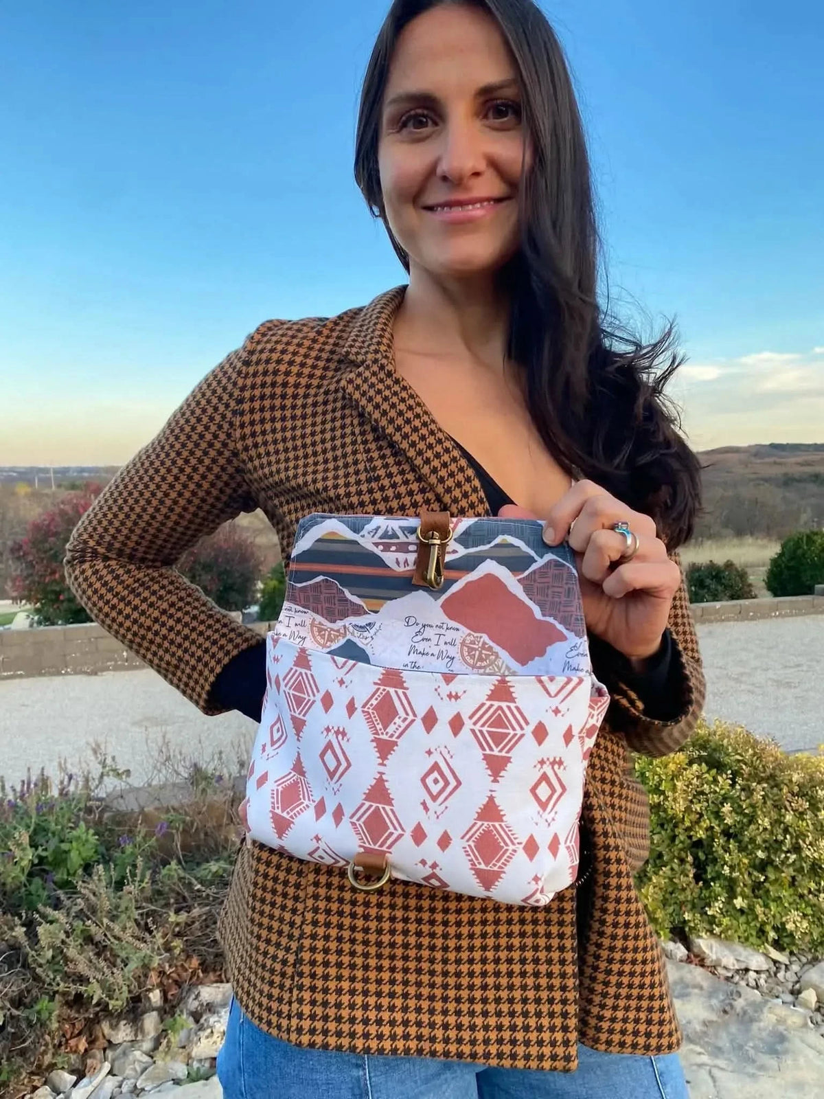 A woman holds a bag with a desert landscape and geometric pattern.