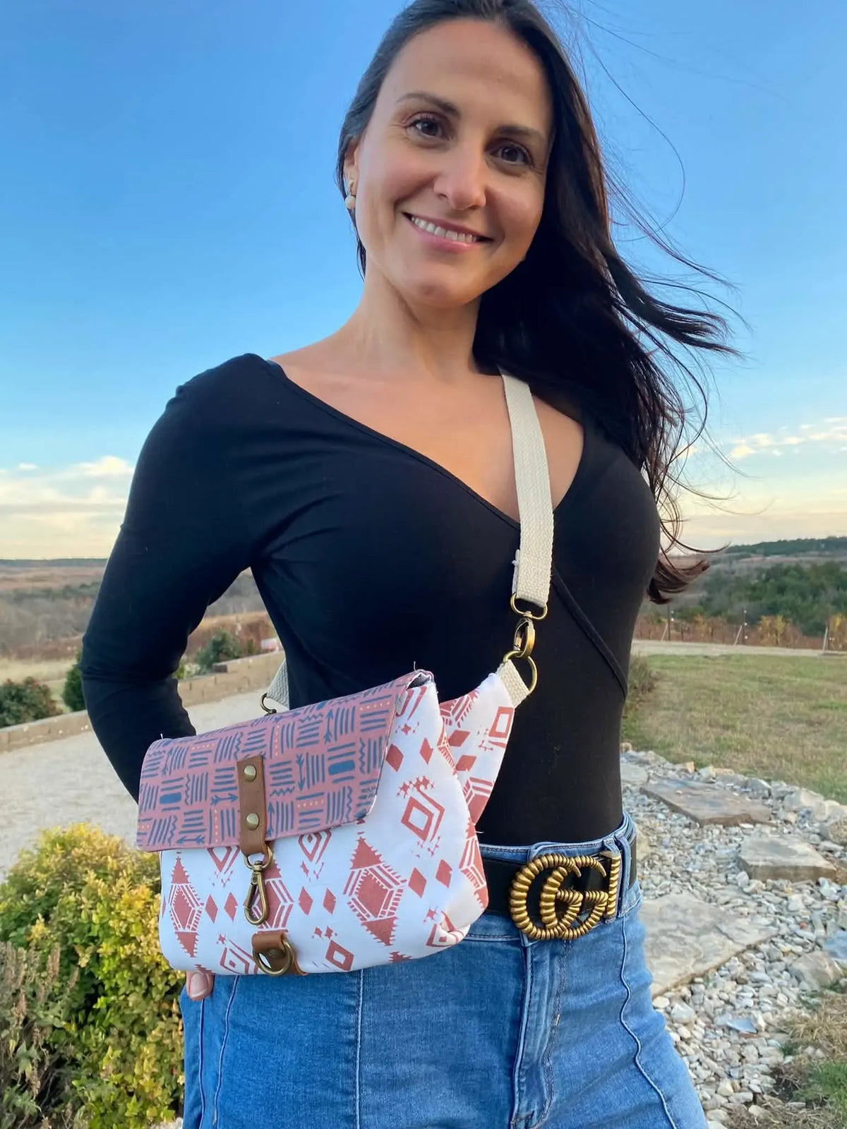 A woman wears a patterned crossbody bag with a black top and jeans.