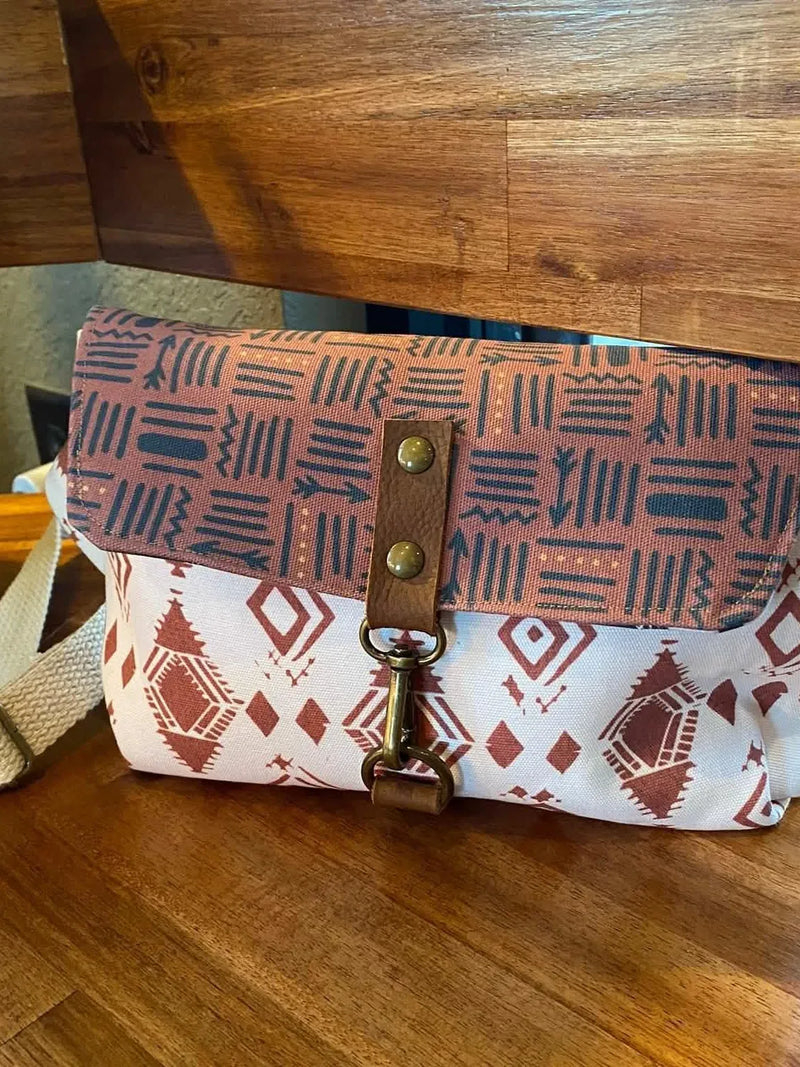 A messenger bag with a brown and white geometric pattern and a leather strap.