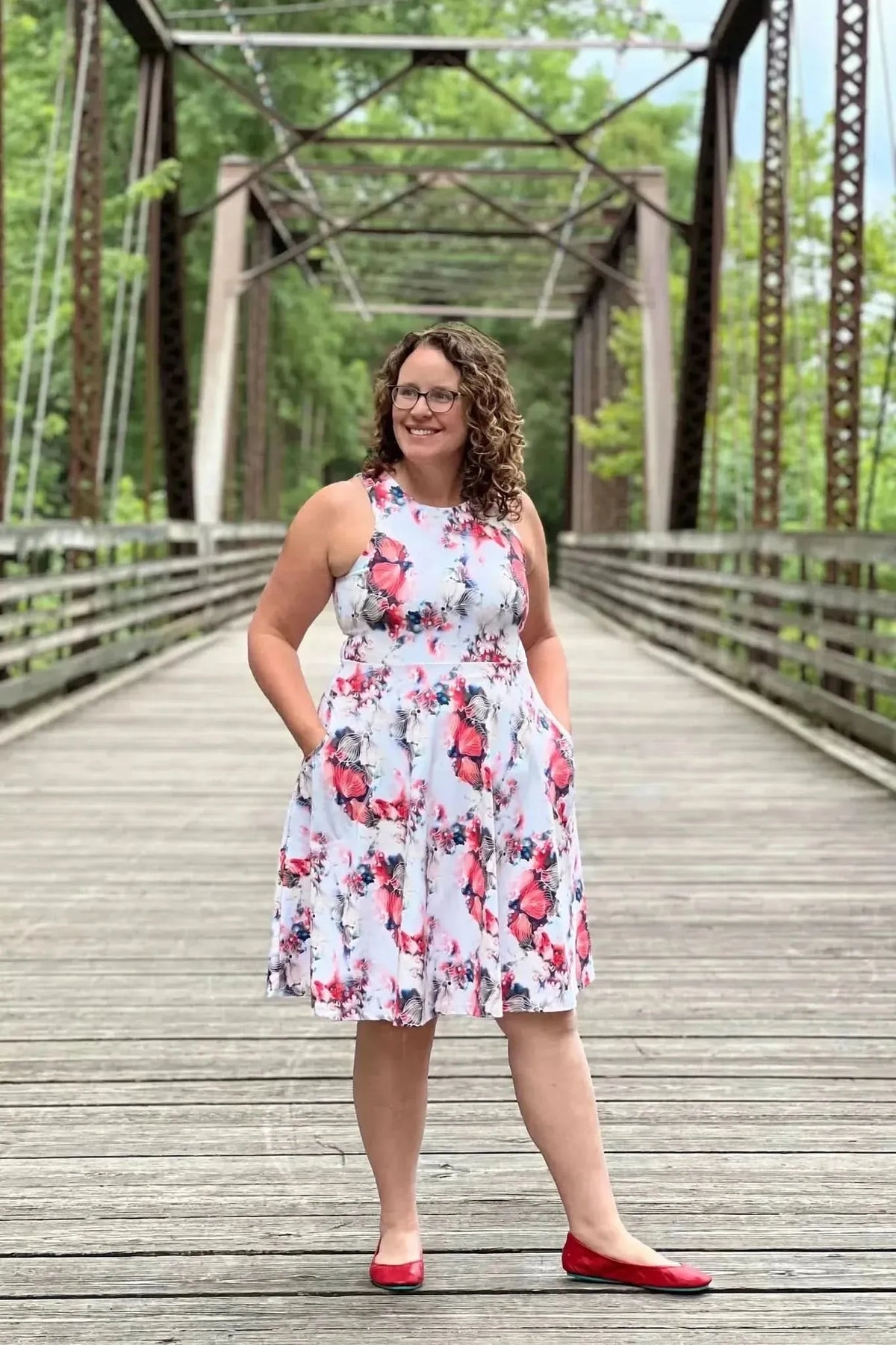 Woman wearing a sleeveless white dress with red floral print on a wooden bridge.