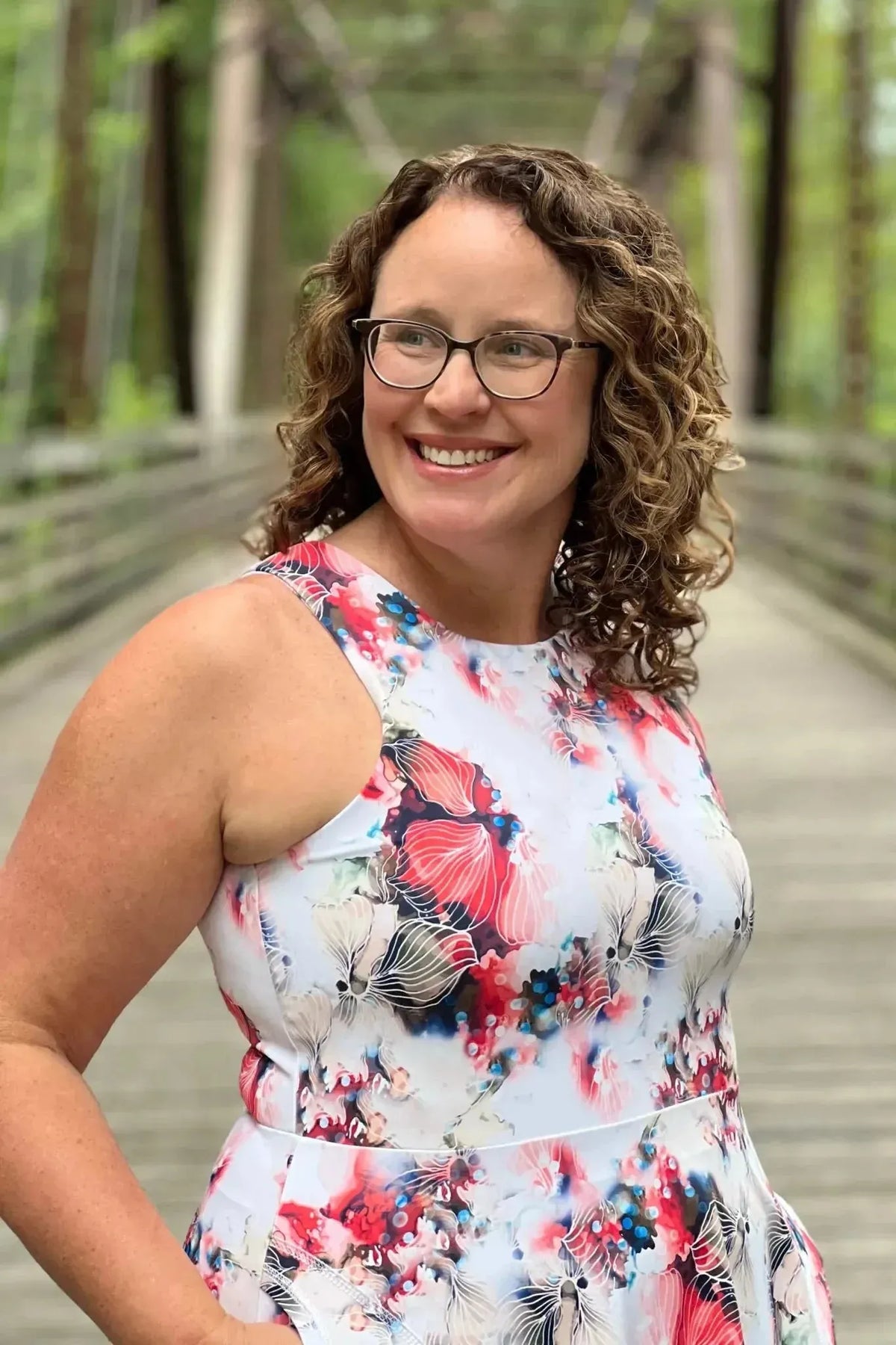 Woman in a floral dress with red, blue, and white flowers, smiling on a bridge.