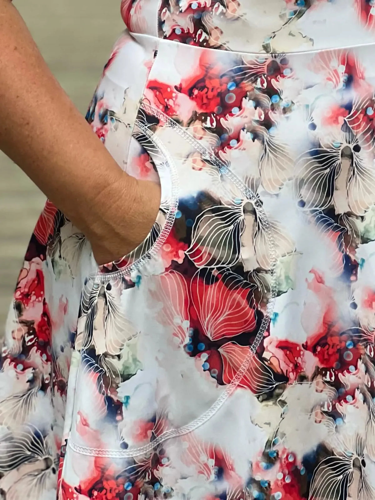 A person wearing a floral skirt with a hand in the pocket.