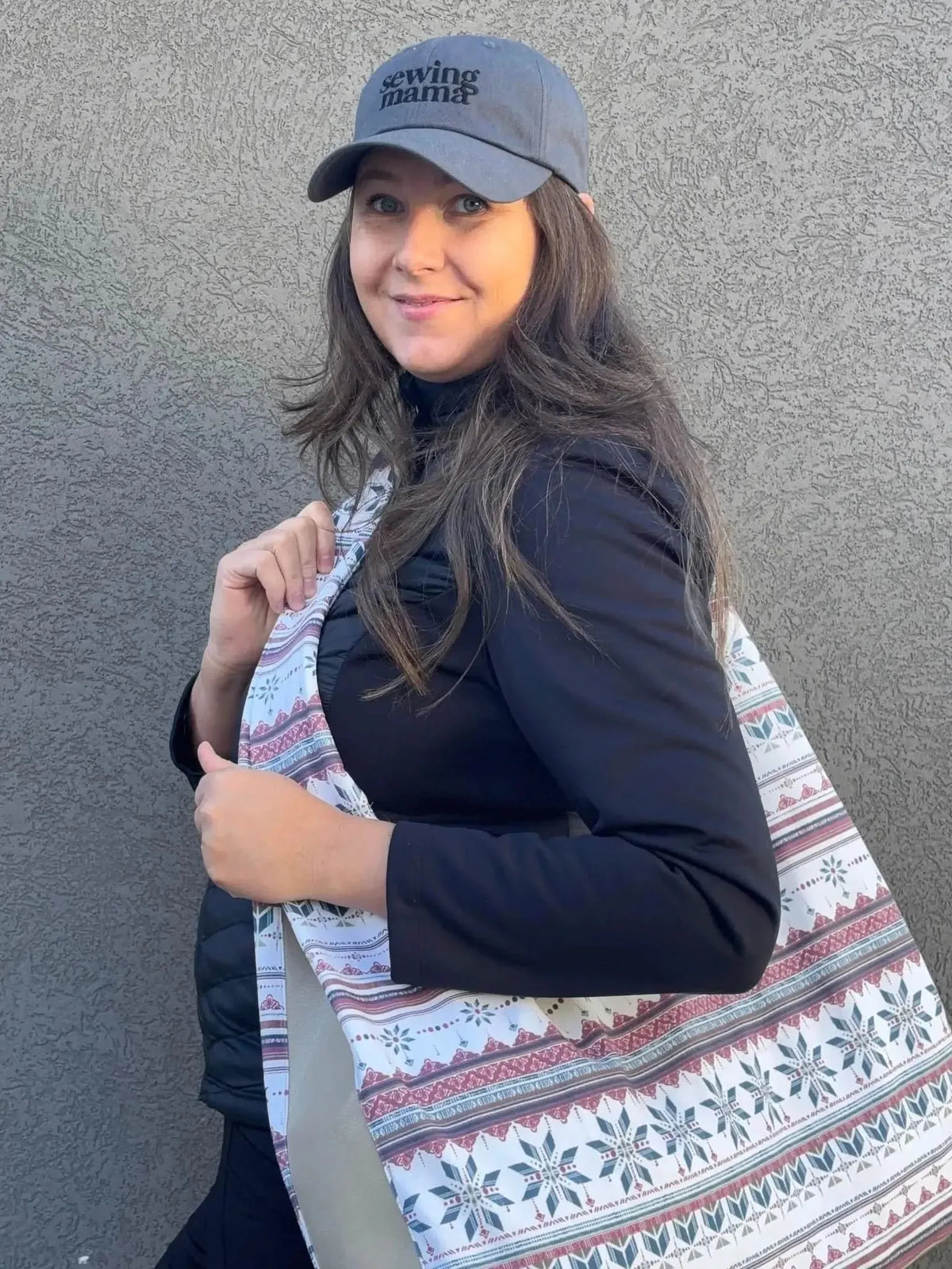 A woman wearing a "sewing mama" hat and a black top holds a patterned fabric.