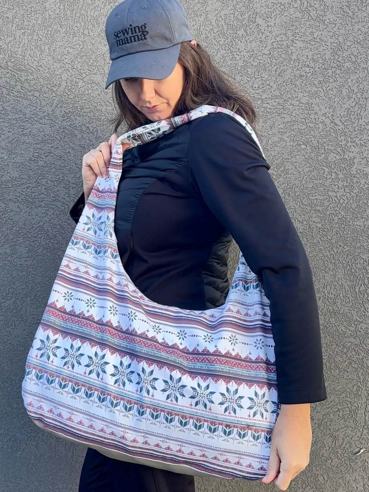 A woman in a black jacket and gray cap holds a white patterned bag.