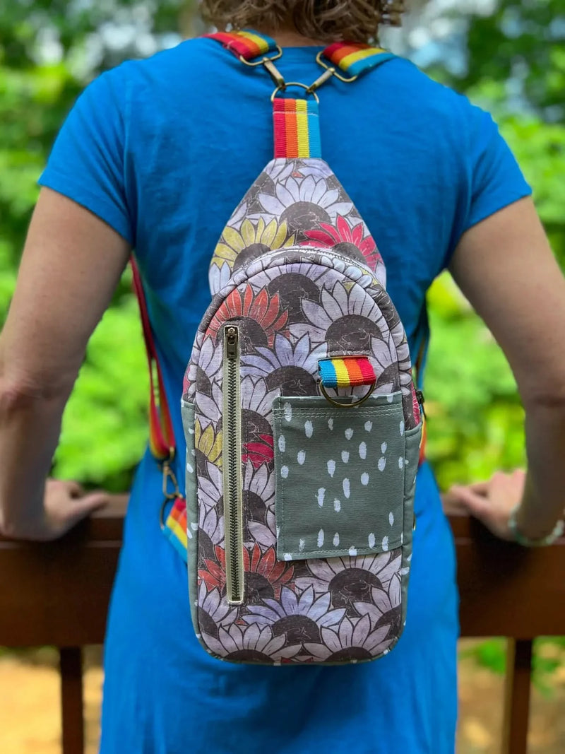 A person wearing a blue shirt and a sunflower-patterned sling bag.