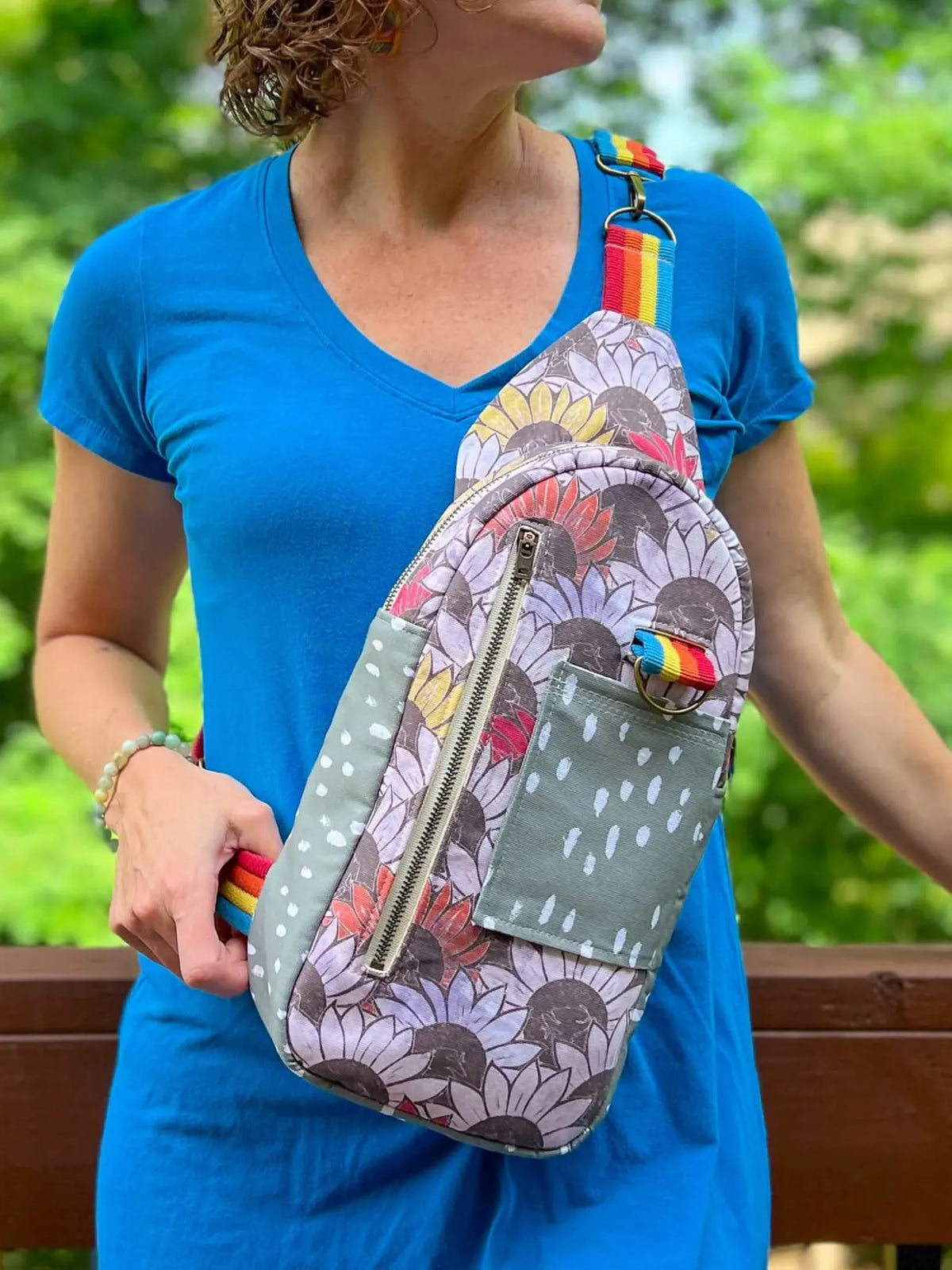 A person wears a sling bag with a sunflower print and rainbow strap.