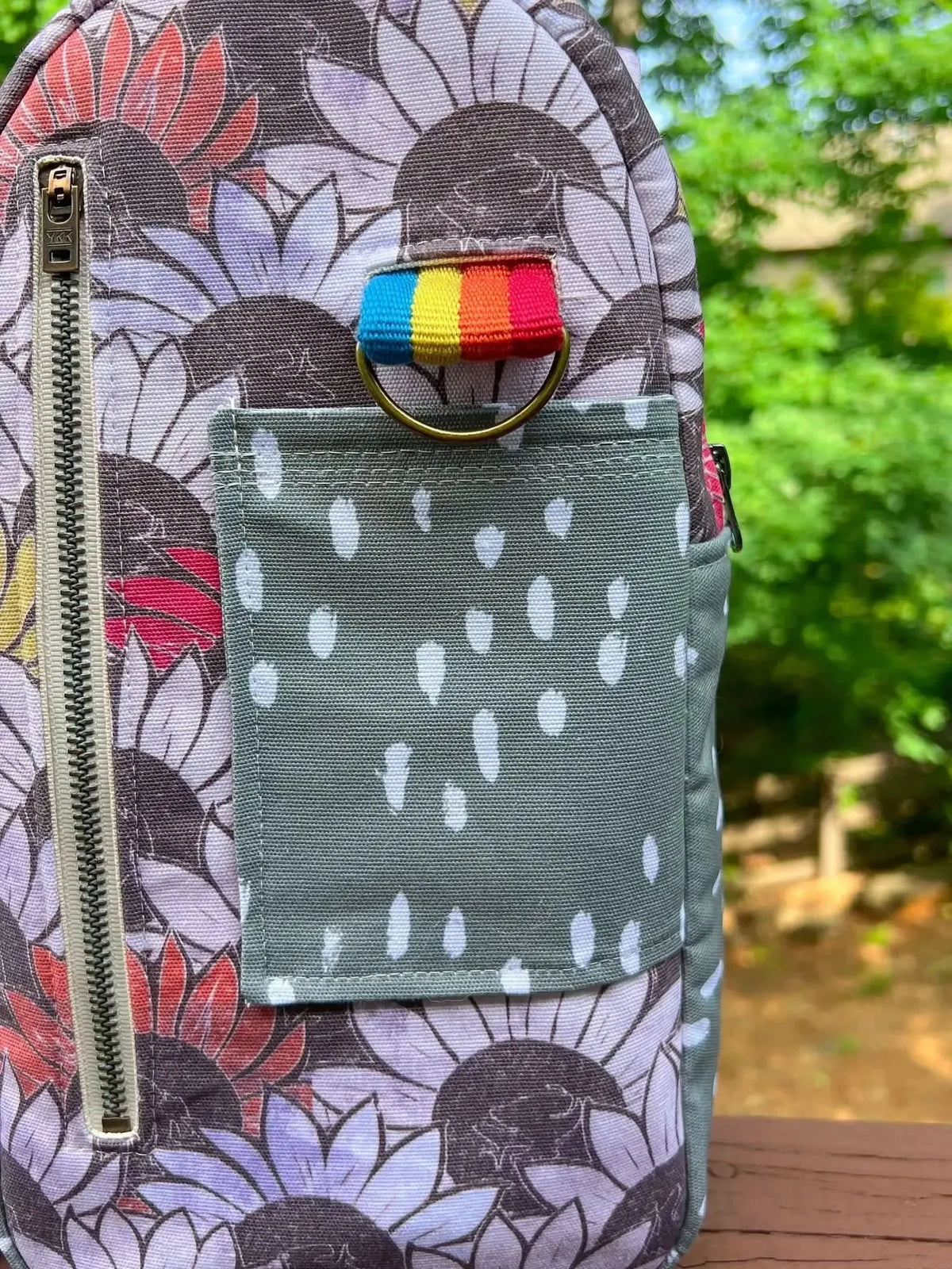A bag with a sunflower pattern, a zipper, a rainbow loop, and a polka dot pocket.