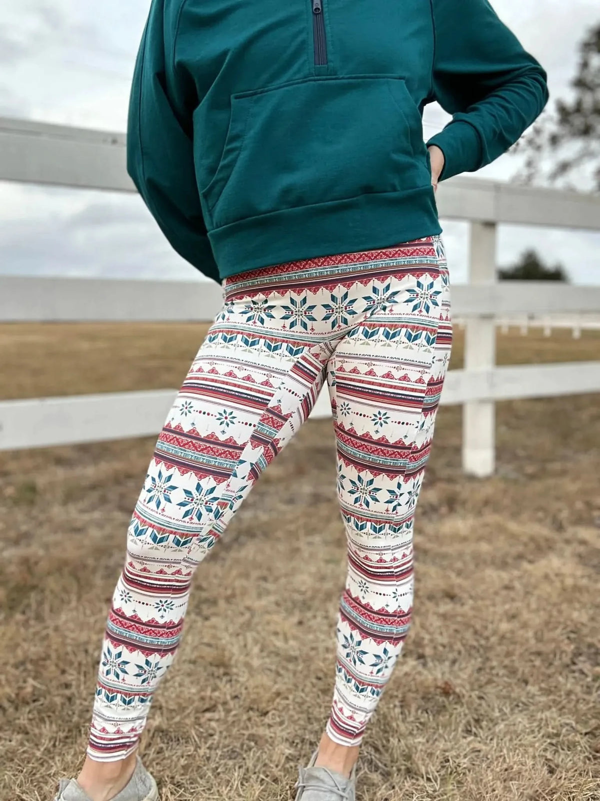 A person wearing a teal hoodie and white leggings with a red and blue snowflake pattern.