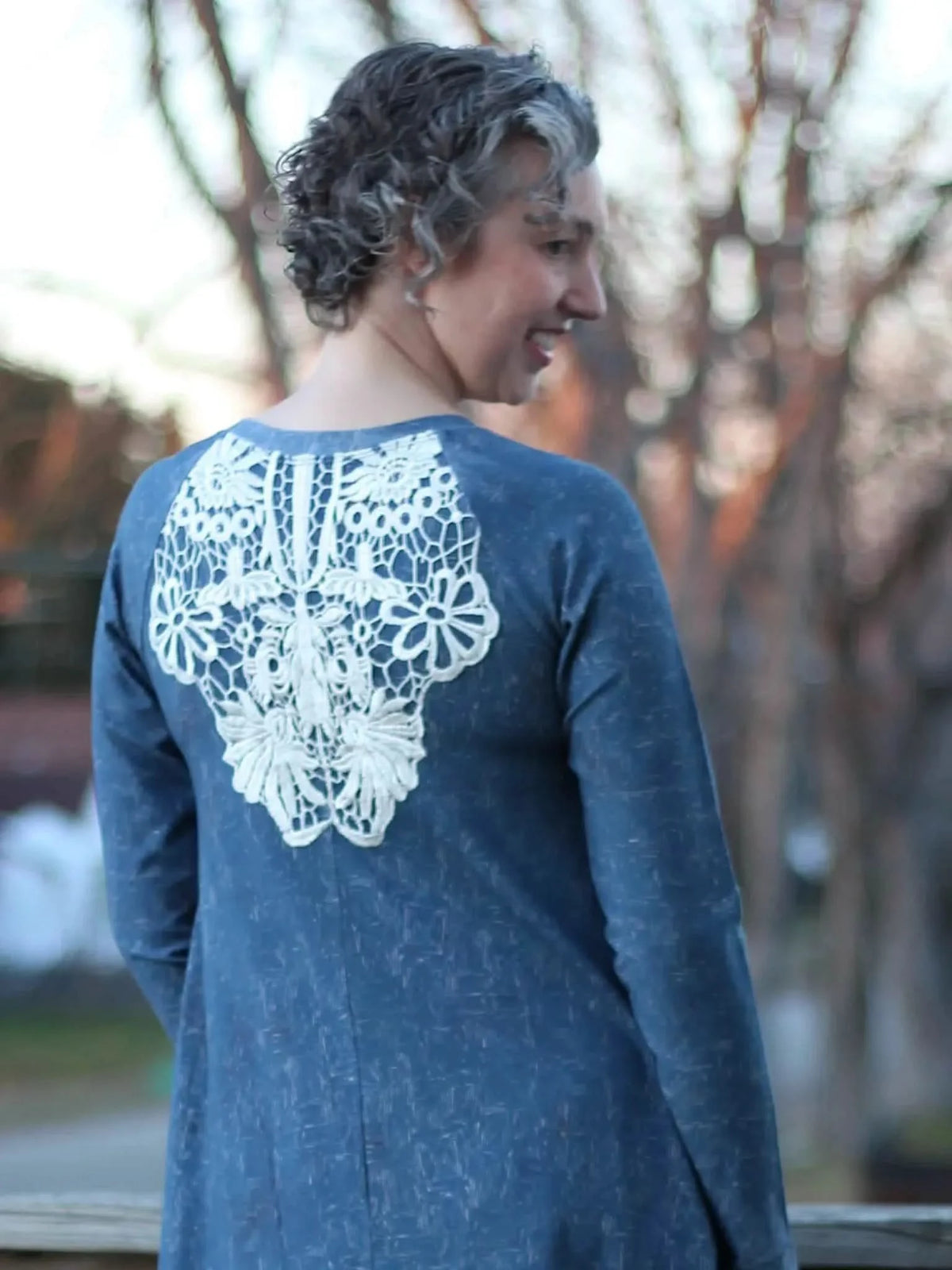 A woman in a blue dress with white lace on the back smiles over her shoulder.